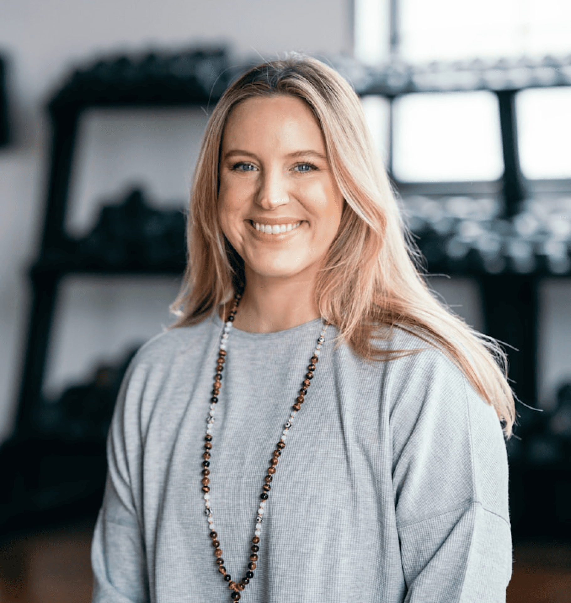 Professional headshot portrait of a smiling woman in grey top with beaded necklace