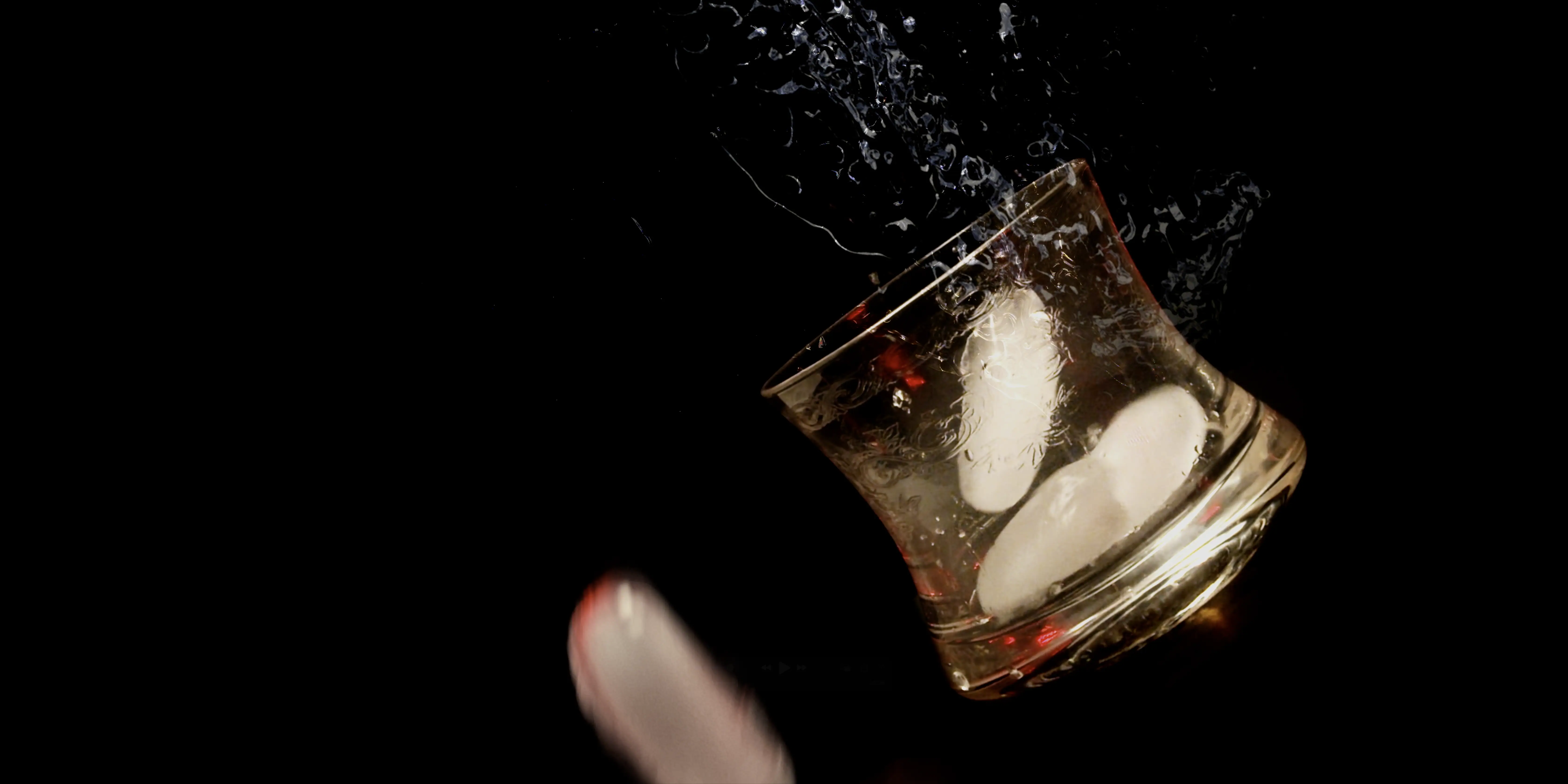 A glass tumbler with ice cubes splashes water against a black background, capturing the motion and energy of the moment.