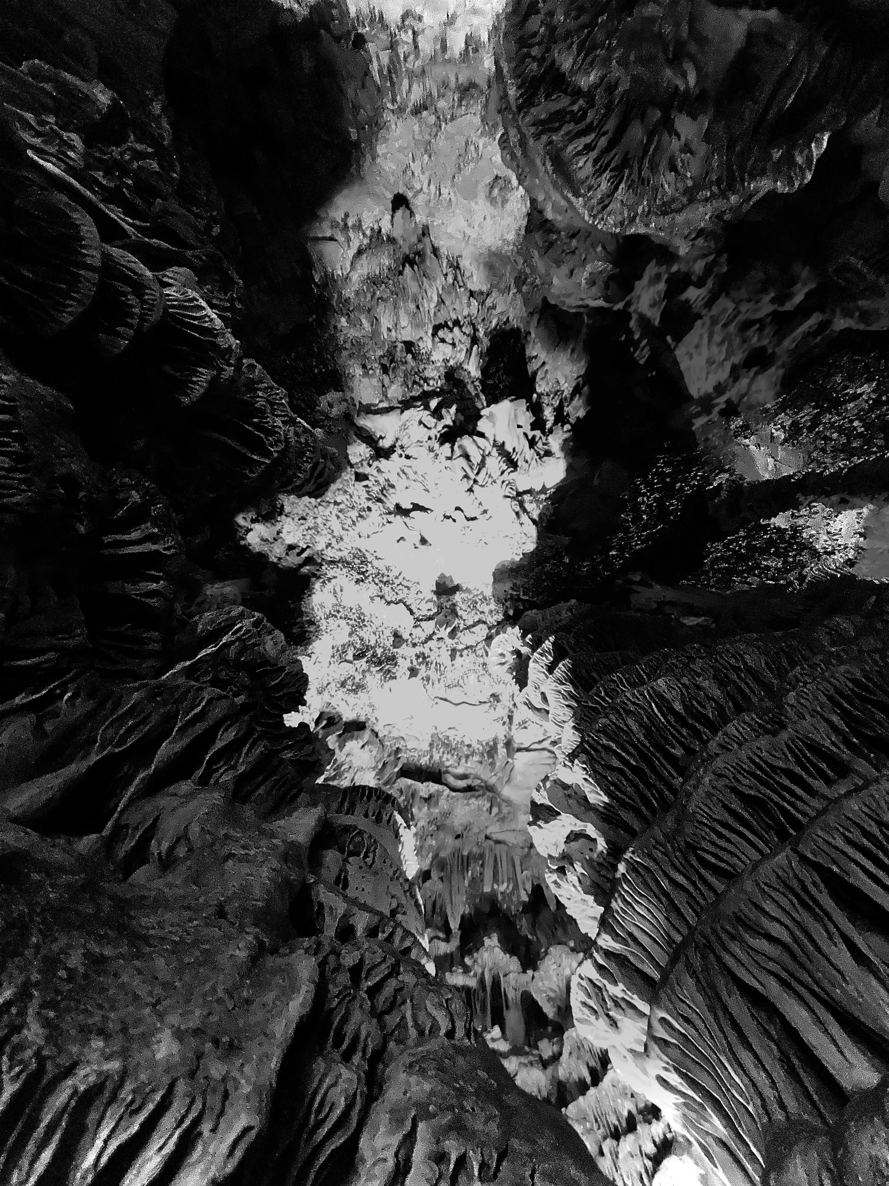 Black and white photo of a cave, from a bottom-up perspective, with rocks of varying textures and shades.