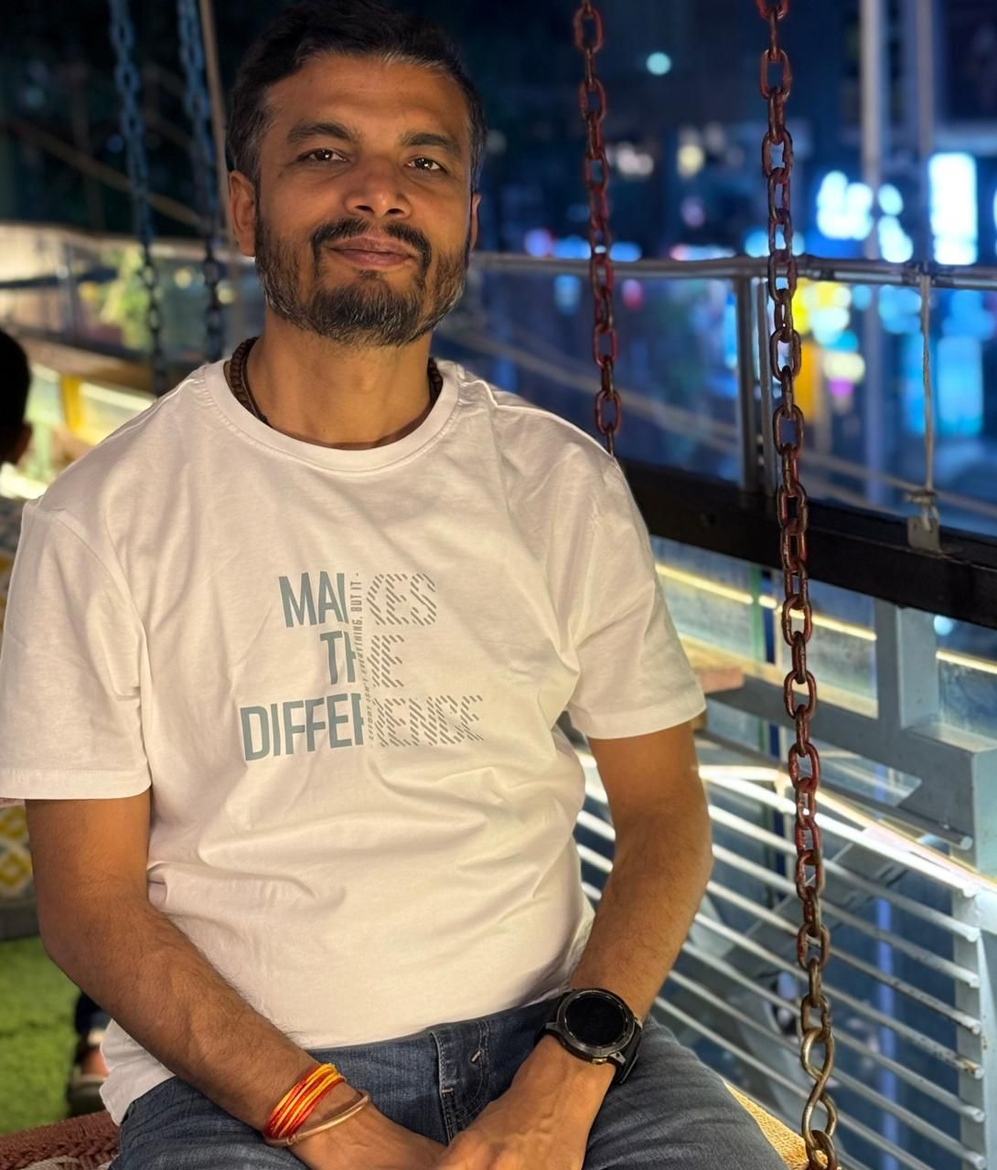 Mature man with glasses and a trimmed beard smiling confidently, standing in warm natural light against a modern backdrop.