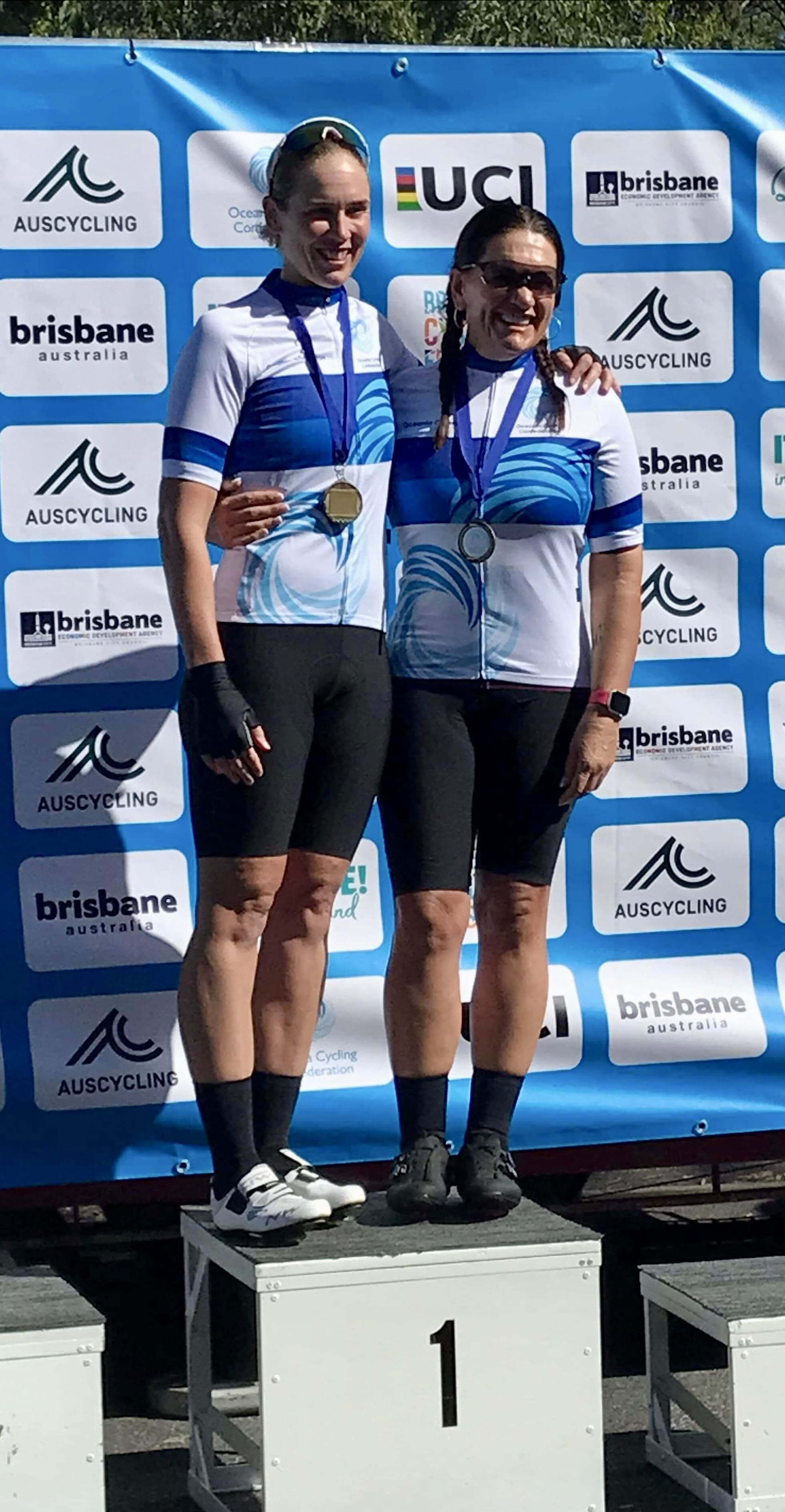 Lily and her pilot, Kelly, standing on the first place podium after winning gold at the Oceania Championships in Brisbane. They wear their championship jerseys.