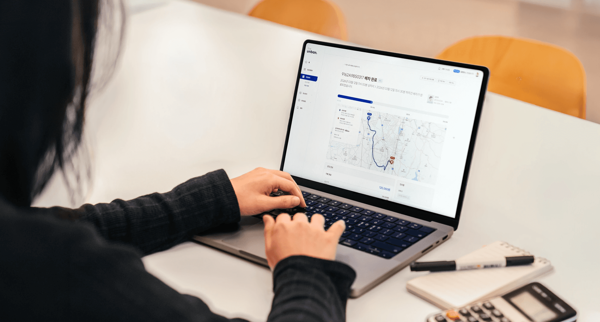 CJ대한통운 더 운반 바로주문 서비스를 소개하는 히어로 이미지로, 노트북 화면에 배차 완료 상태의 운송 경로 지도와 운임 정보가 표시되어 있습니다. AI가 산출하는 최적 운임으로 전국 차주 매칭과 실시간 관제까지 한 번에 처리할 수 있음을 안내합니다.