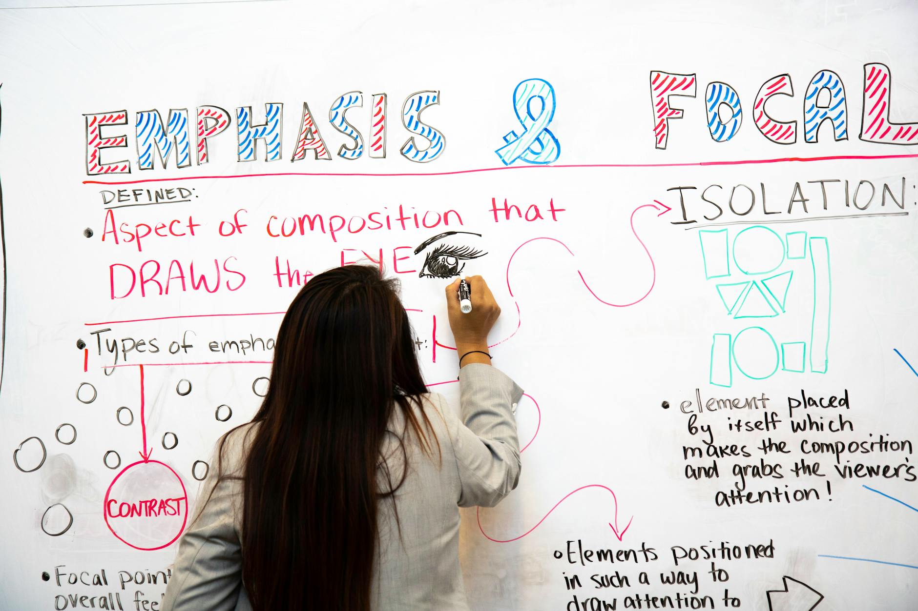 A close-up shot of a teacher's hands holding a colorful planning journal and a wooden pointer over a desk.