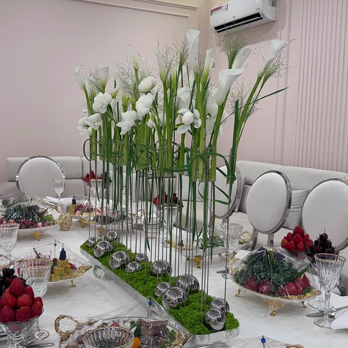 Formal dining table with tall white floral centerpieces, crystal glassware, fruits, and appetizers, surrounded by ornate chairs in a classic, luxurious room.