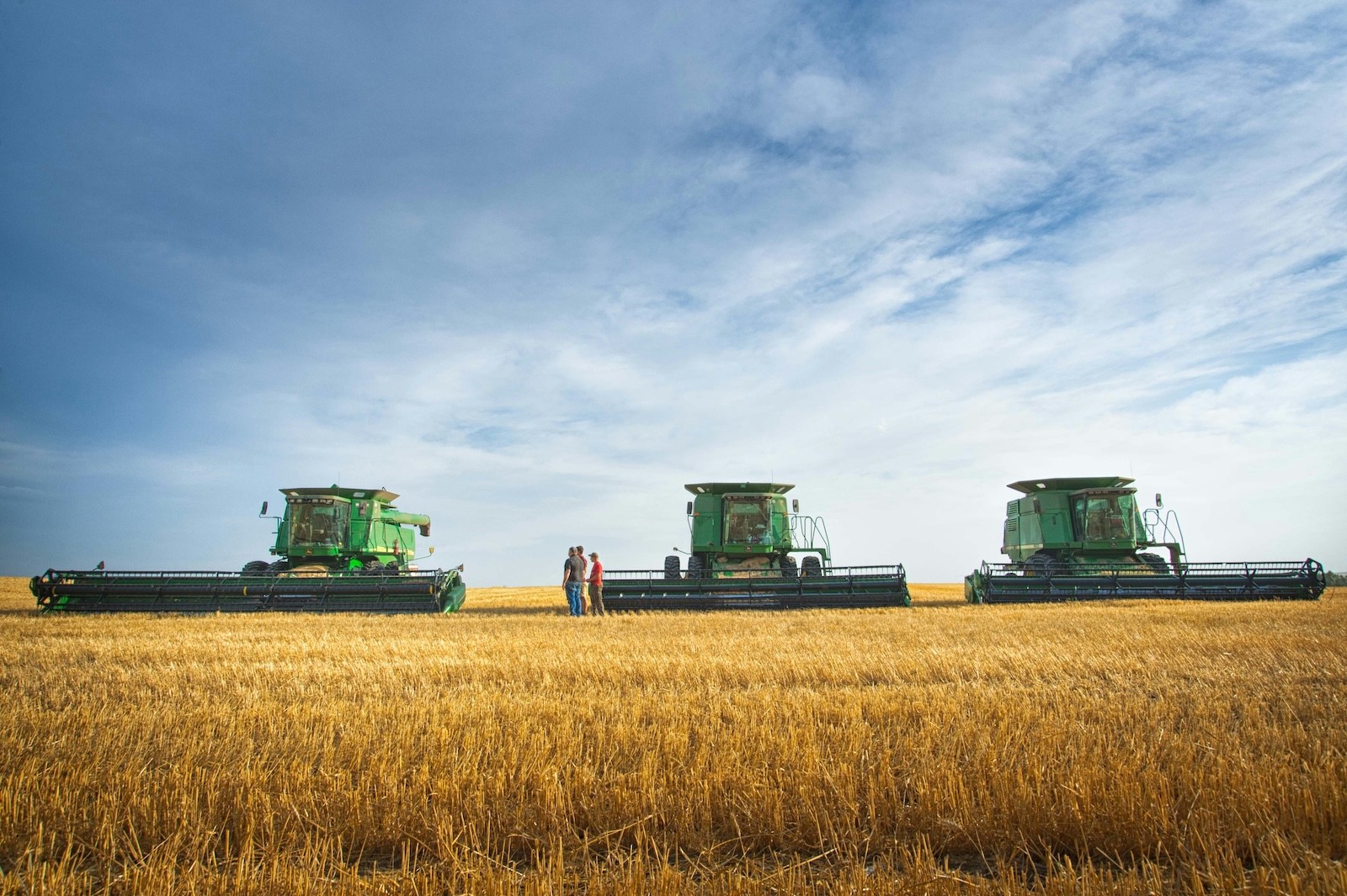 a couple of people standing in a field next to a couple of large green farm