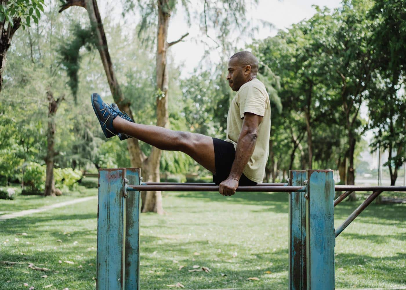 Man outdoors holding dip bar with hands while raising legs above dip bar to showcase calisthenics workouts