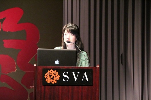 a woman giving a speech from a stand in the "designer as" thesis presentation