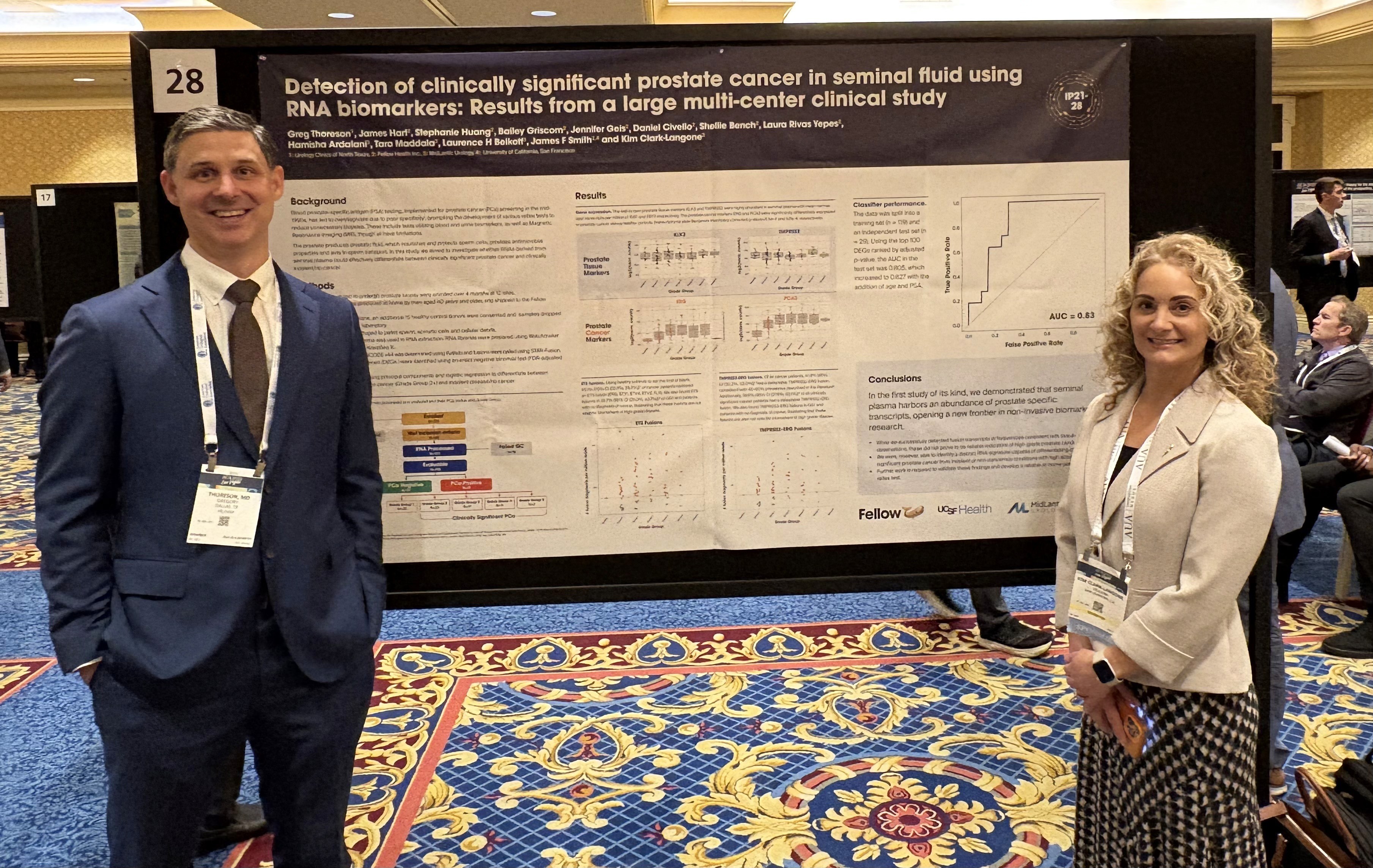 Two professionals stand in front of a research poster presented by Fellow