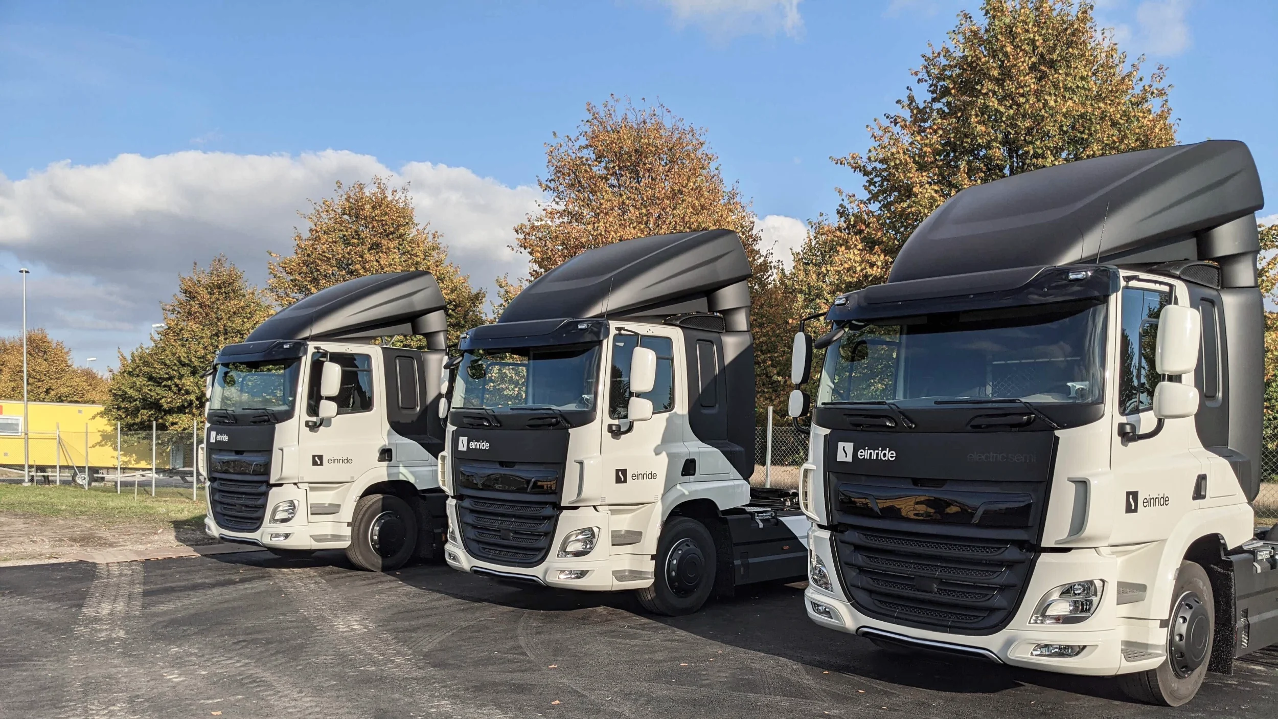 The front of three Einride electric trucks parked outside on a parking lot.