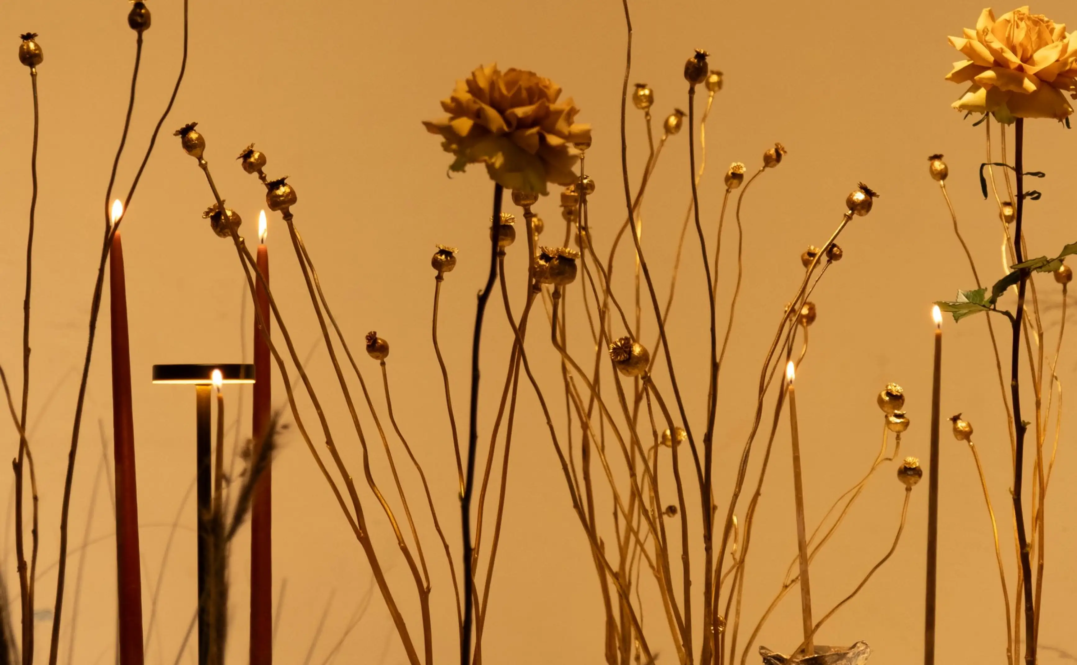 Instalación floral con velas y tallos dorados para proyecto artístico de interiorismo, logrando una atmósfera cálida y escultórica.