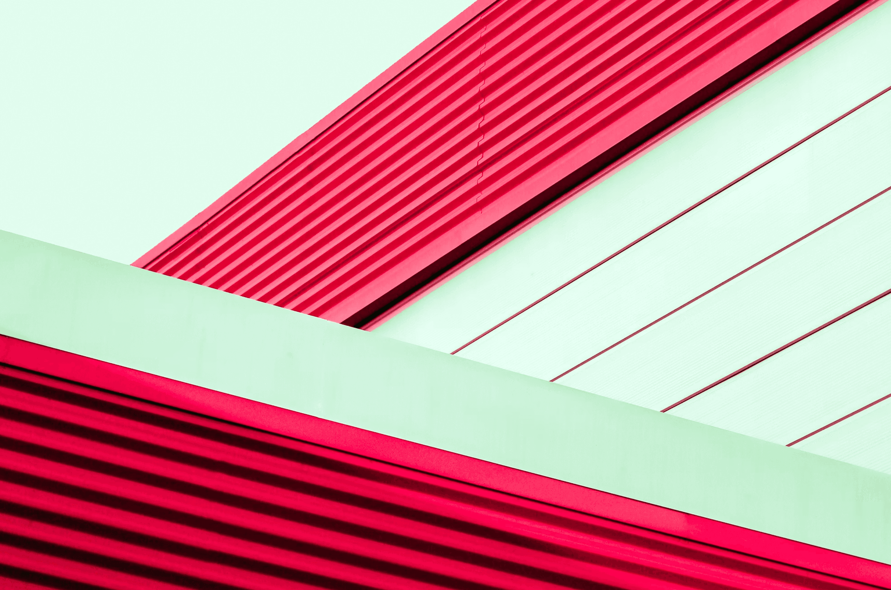 Alt text: Abstract architectural detail with bold red ribbed panels intersecting soft mint-green surfaces, creating clean lines and sharp contrasts that feel modern, structured, and deliberately minimal.