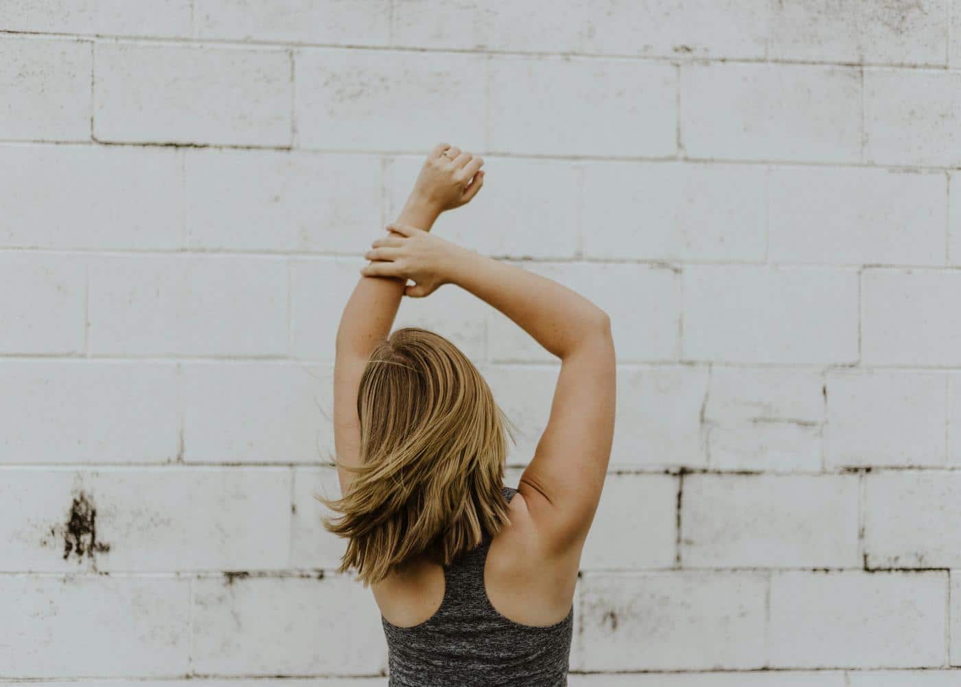 Woman outside doing forward head posture exercies with arms above her head