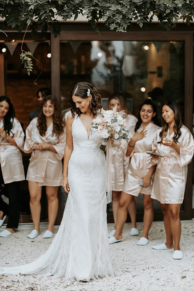 Braut im Spitzenkleid mit Brautstrauß umgeben von Brautjungfern in rosé Satin-Roben, Getting Ready Hochzeitsfotografie von Eva Sitko