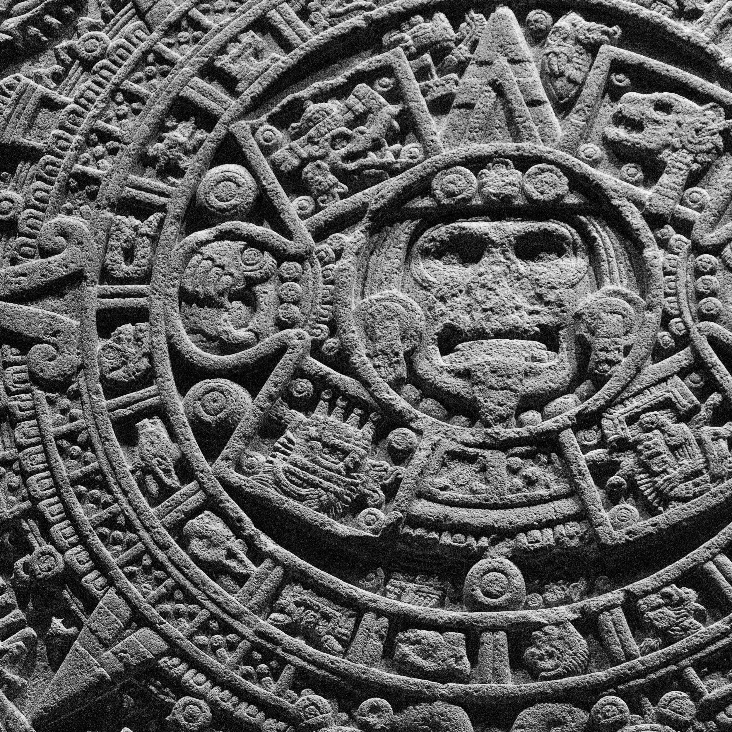 Detailed black and white image of the Aztec Sun Stone (Piedra del Sol), capturing the central face of Tonatiuh surrounded by intricate symbols representing cosmic and mythological elements.
