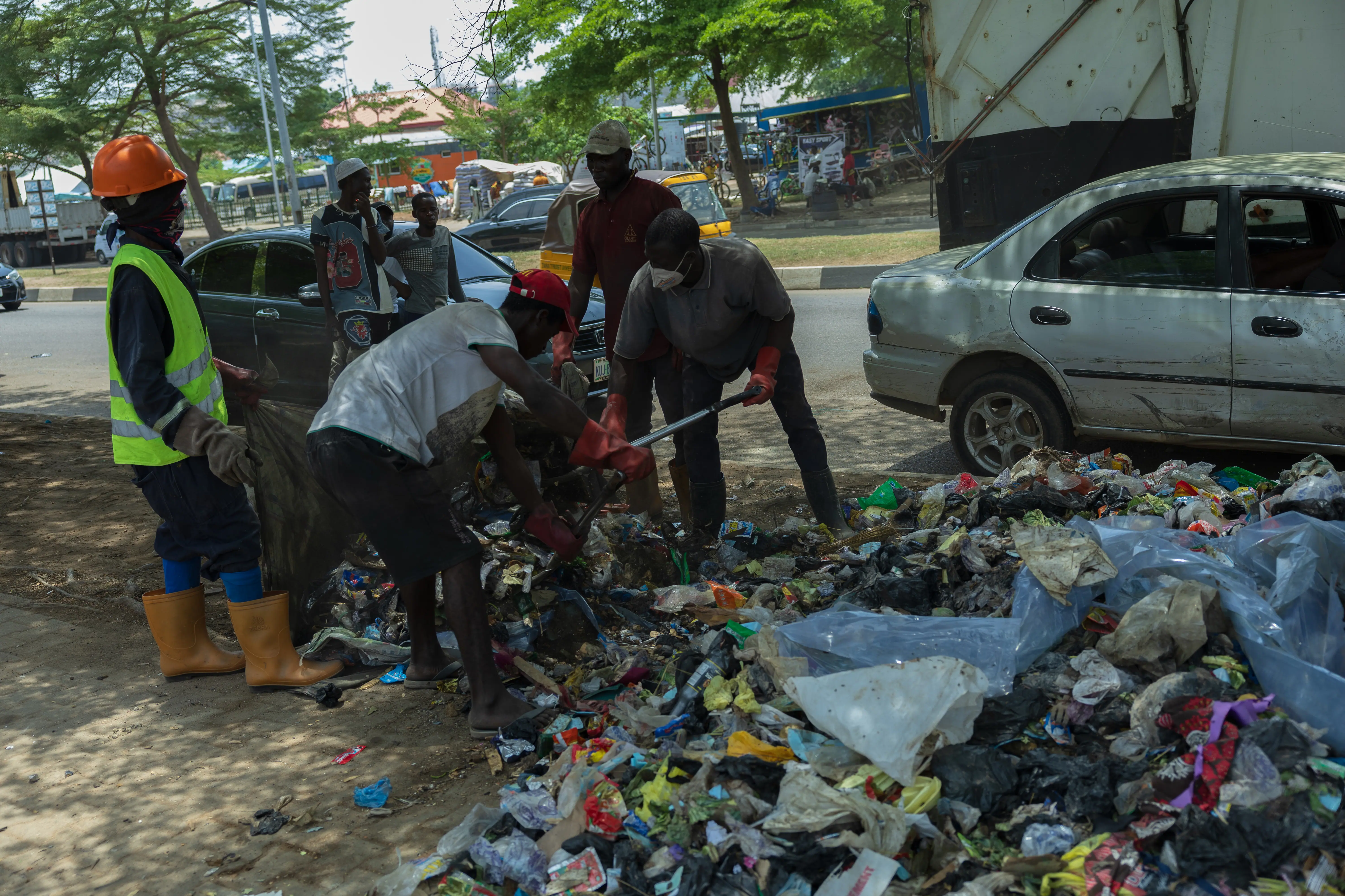 Waste management crew clearing a roadside rubbish dump using shovels and collection sacks.