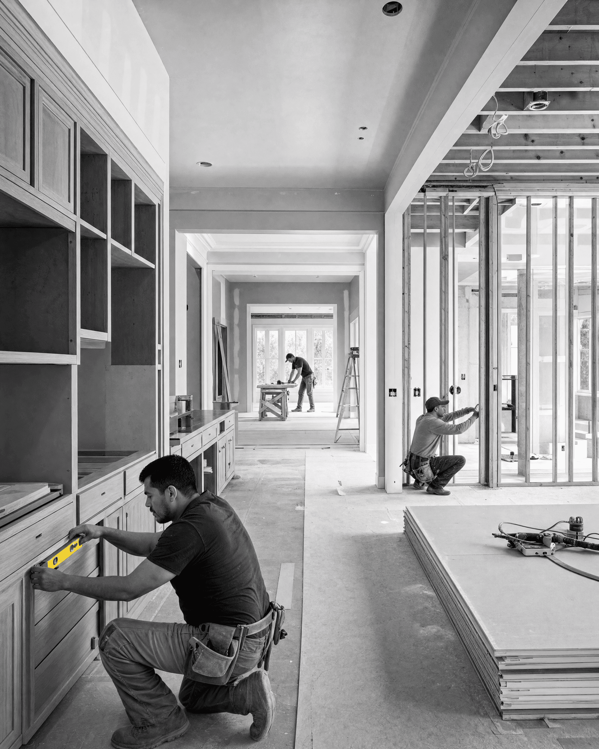 Multi-room renovation in progress with cabinetry, exposed framing, drywall, and crews working across connected spaces.