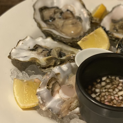 Isang plato ng mga talaba sa yelo na may mga hiwa ng limon at isang maliit na mangkok ng diced na sibuyas na sawsawan.