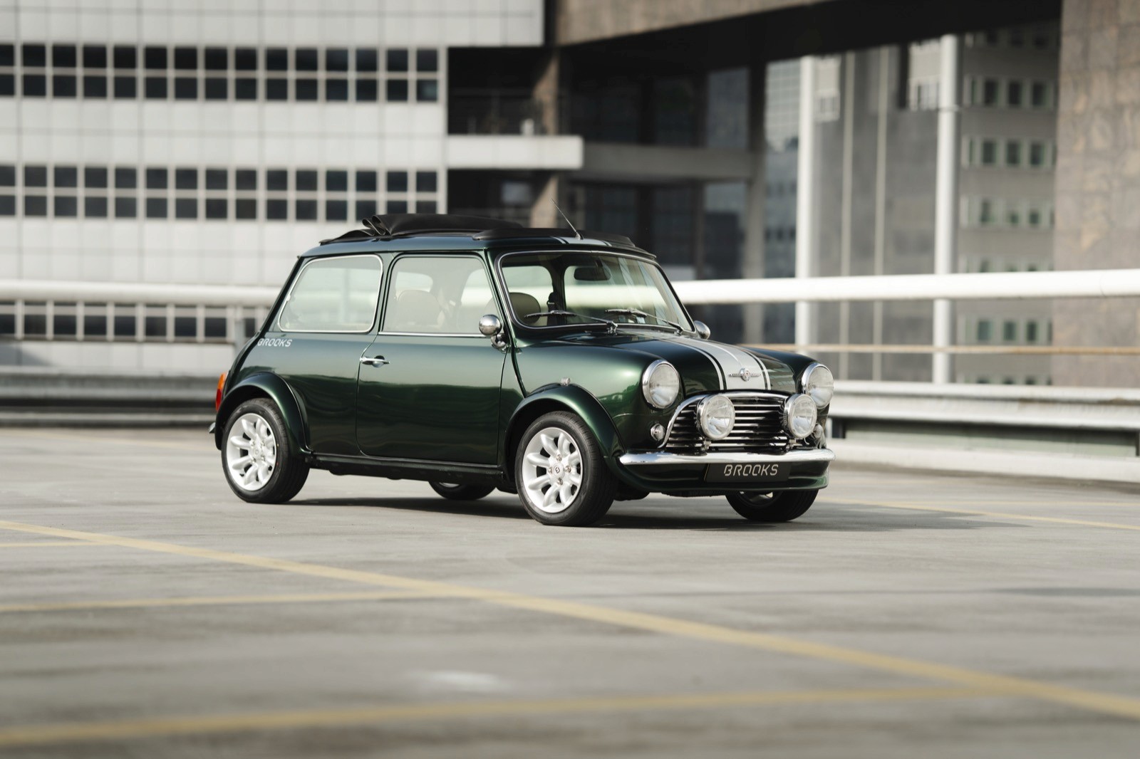 A classic green car parked near a modern building with large windows. Bright daylight enhances the scene.