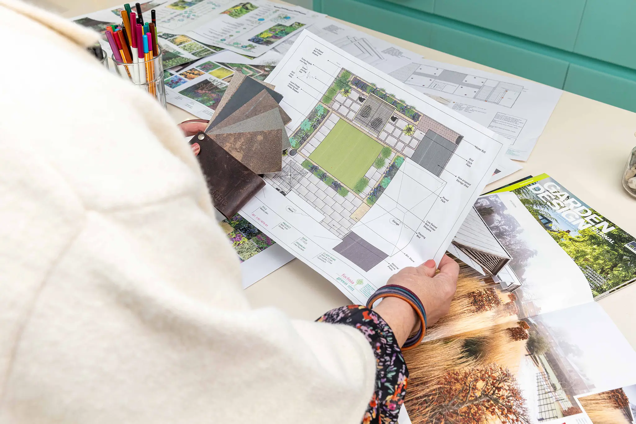 A person reads a newspaper while seated at a table, surrounded by various papers and items.