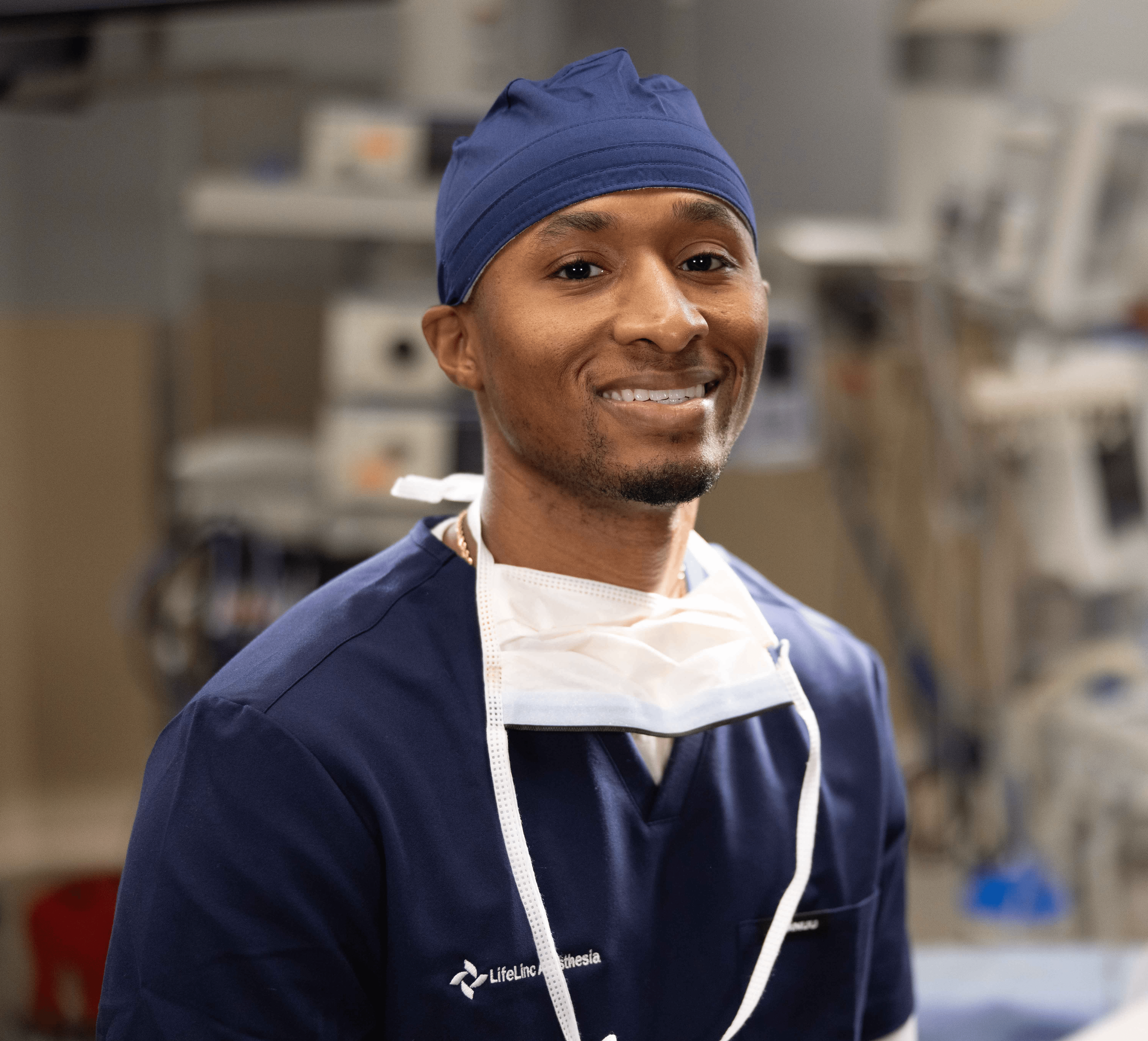 A confident CRNA in navy scrubs and a surgical cap smiles in a clinical setting, representing LifeLinc's commitment to anesthesia provider well-being, leadership development, and professional growth resources