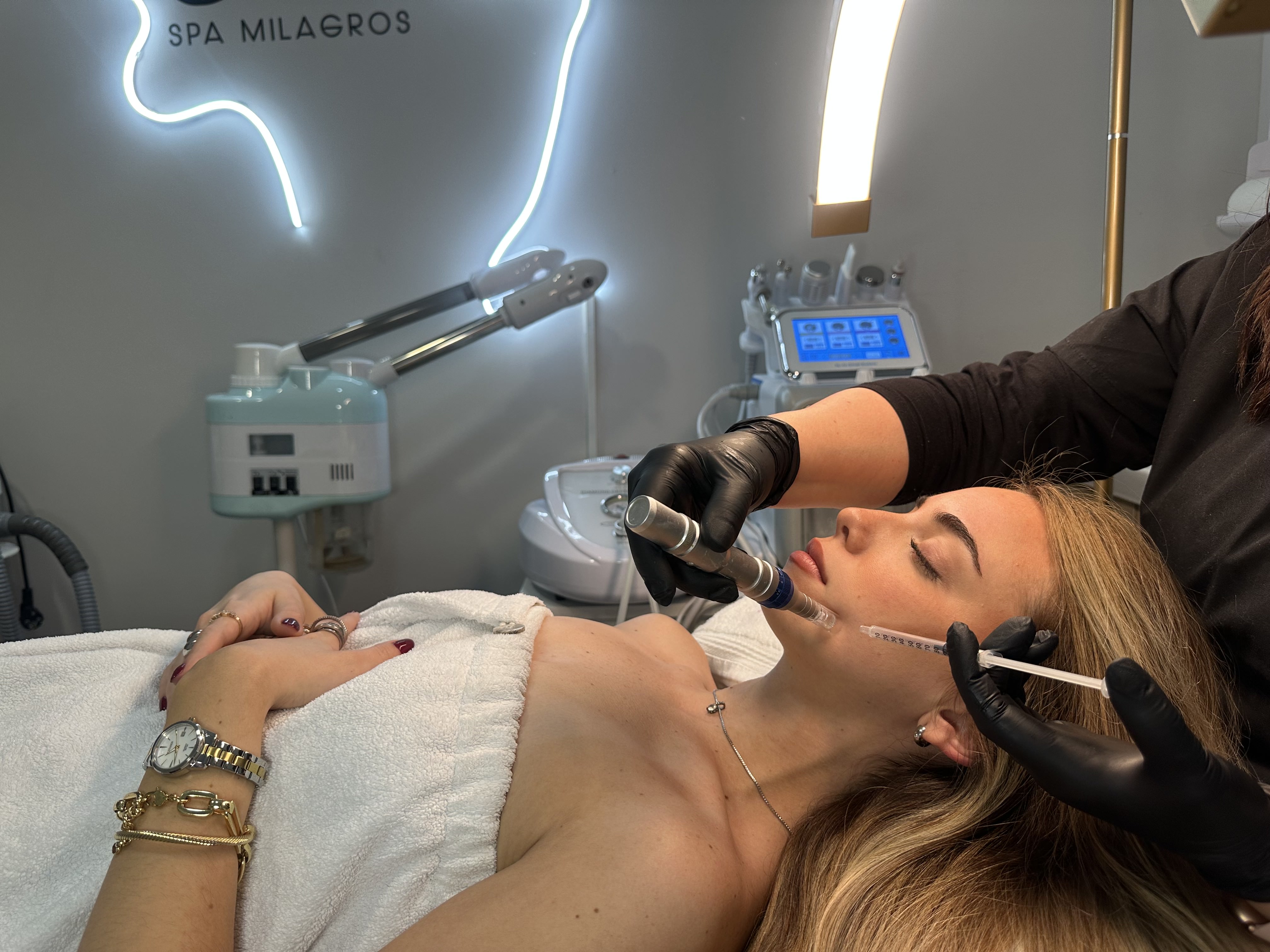 A woman lying down with a towel wrapped around her head, her face glowing with facial oil. She has a peaceful expression, enjoying a skincare treatment.
