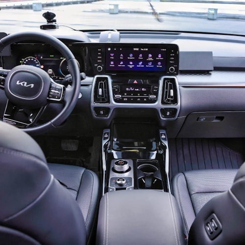 Interior de un coche moderno, con un logotipo de Kia en el volante, una gran pantalla táctil y asientos de cuero.