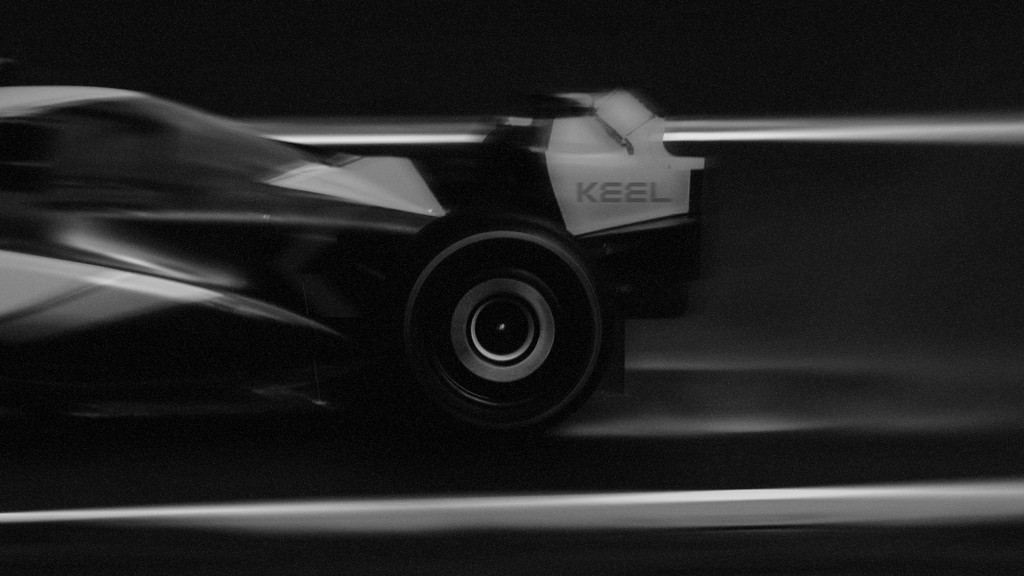 Black and white motion blur of a race car in side view, emphasizing speed and aerodynamic form.