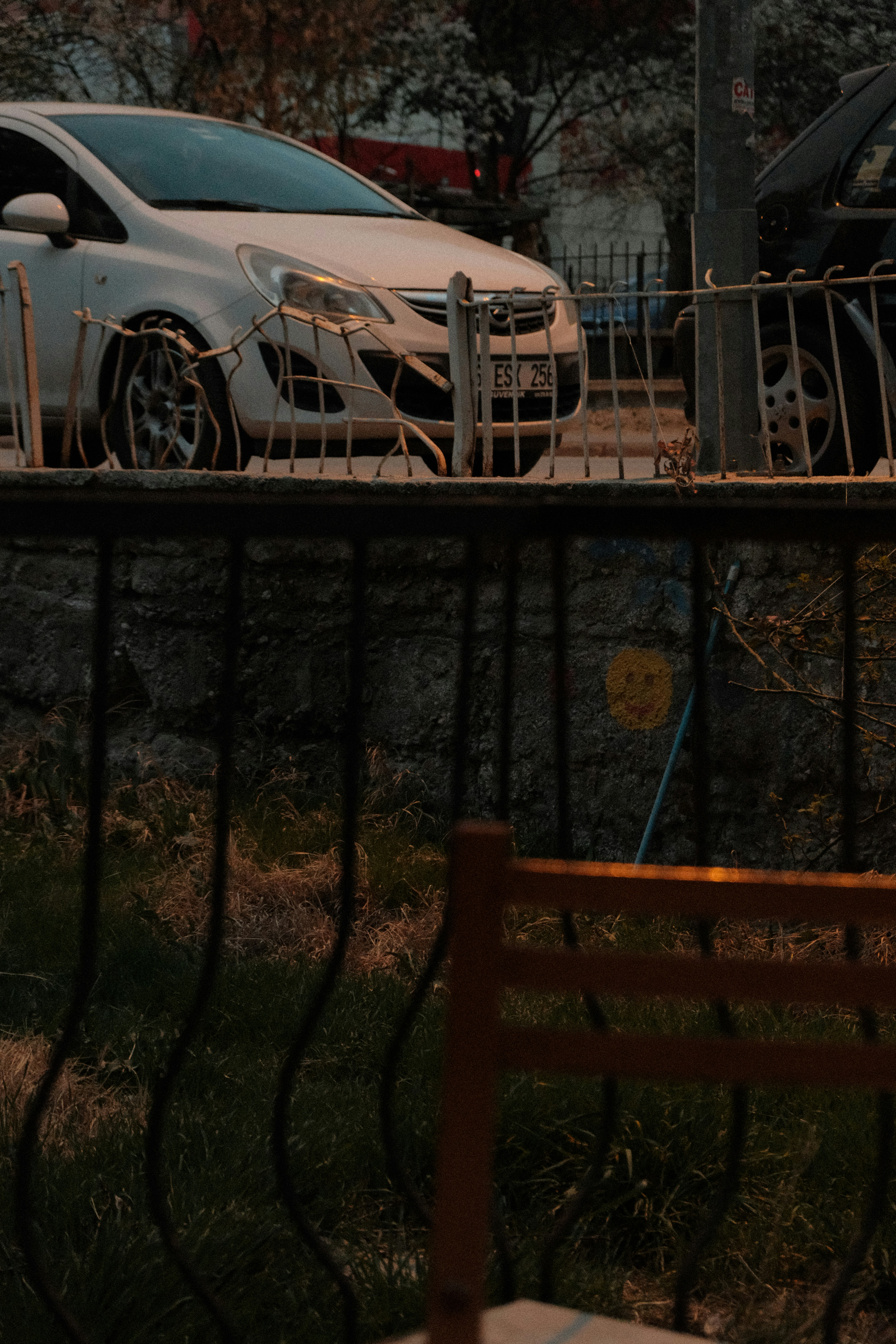 A white car sits near a metal fence.