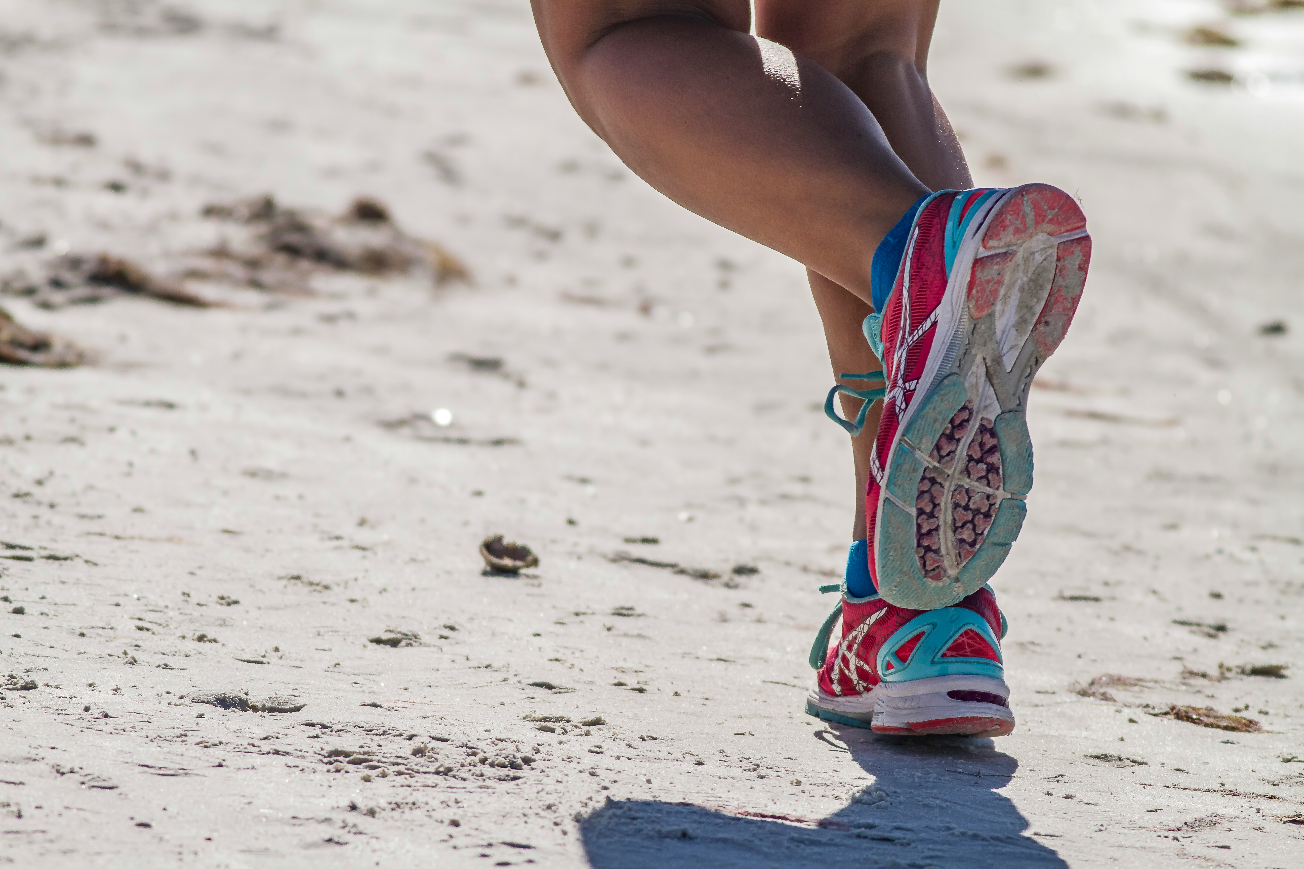 woman in white red and blue sneakers sitting on white sand during daytime