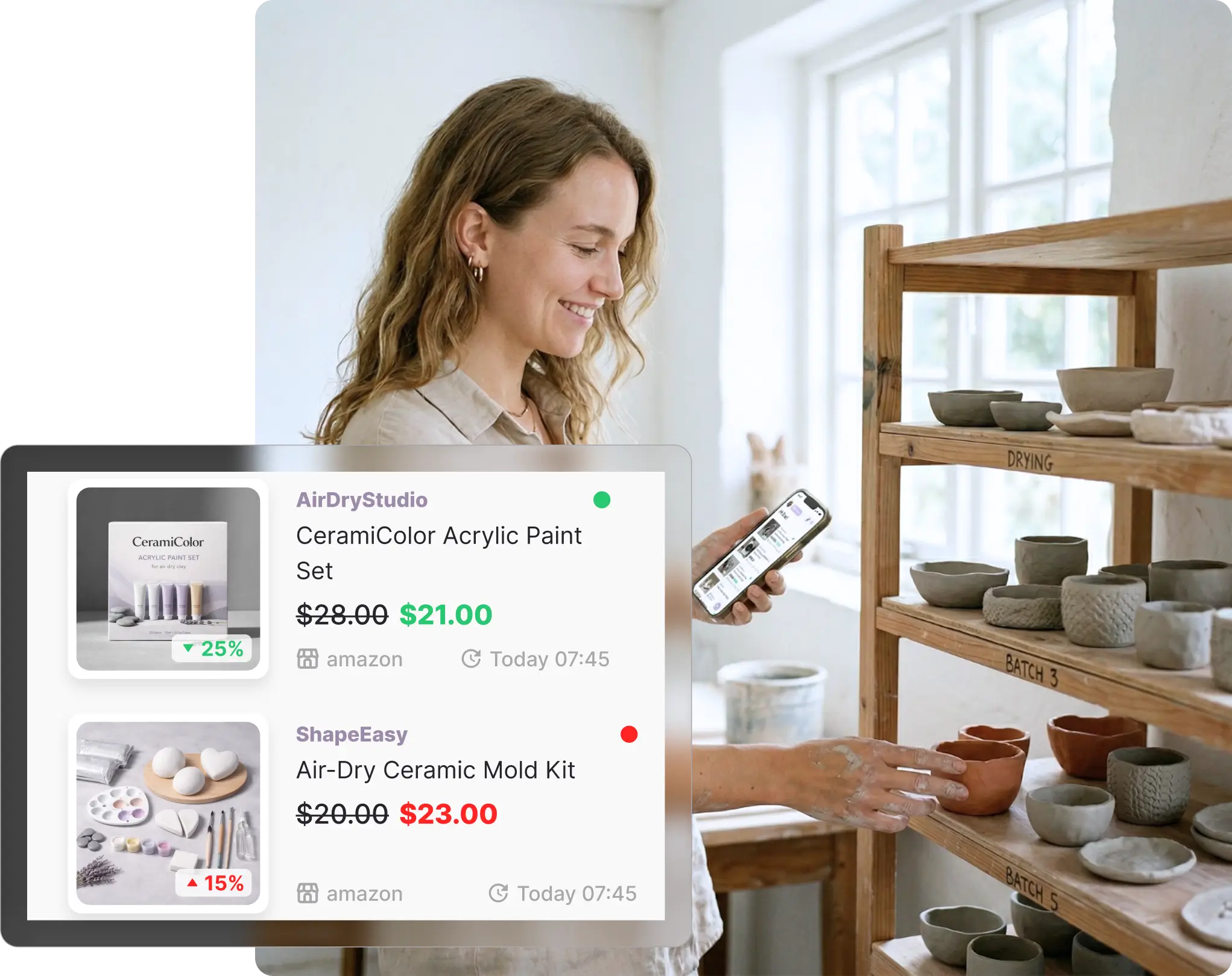 Woman in a ceramics workshop checking her phone, with clay pots and craft supplies on wooden shelves behind her, viewing her Amazon watchlist on Whisprice showing an acrylic paint set down 25% and a ceramic mold kit up 15%.