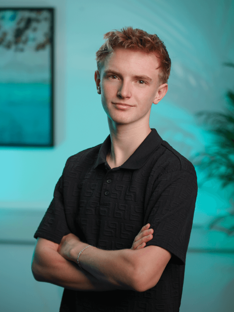 A man with glasses and a brown shirt, crossing his arms.