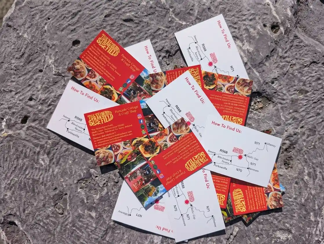 A scattered pile of vibrant, high-contrast business cards for The Strawberryfield resting on a natural stone surface, showcasing the new offline brand identity.