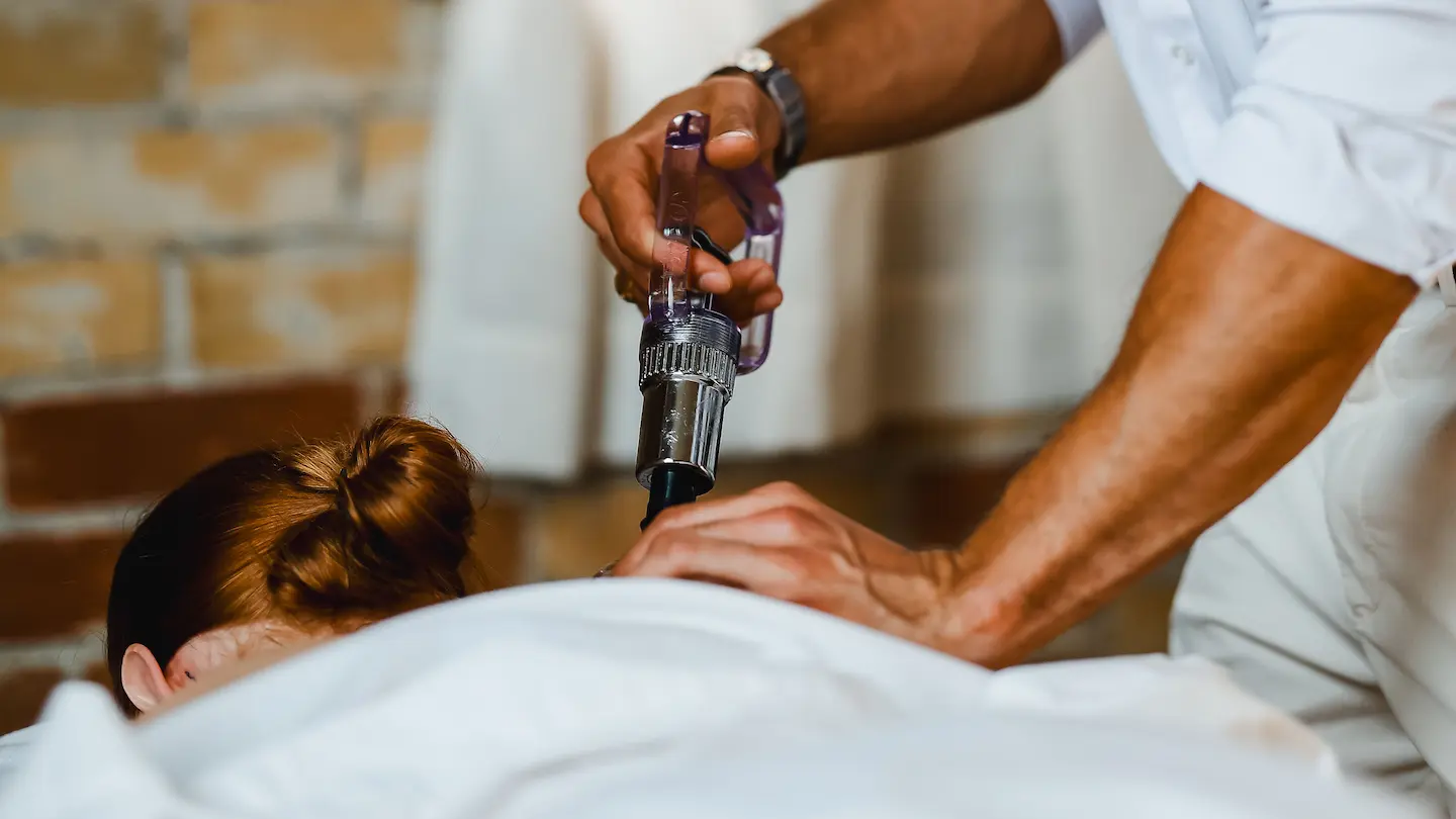 Practitioner applying a handheld therapy device to a patient's upper back