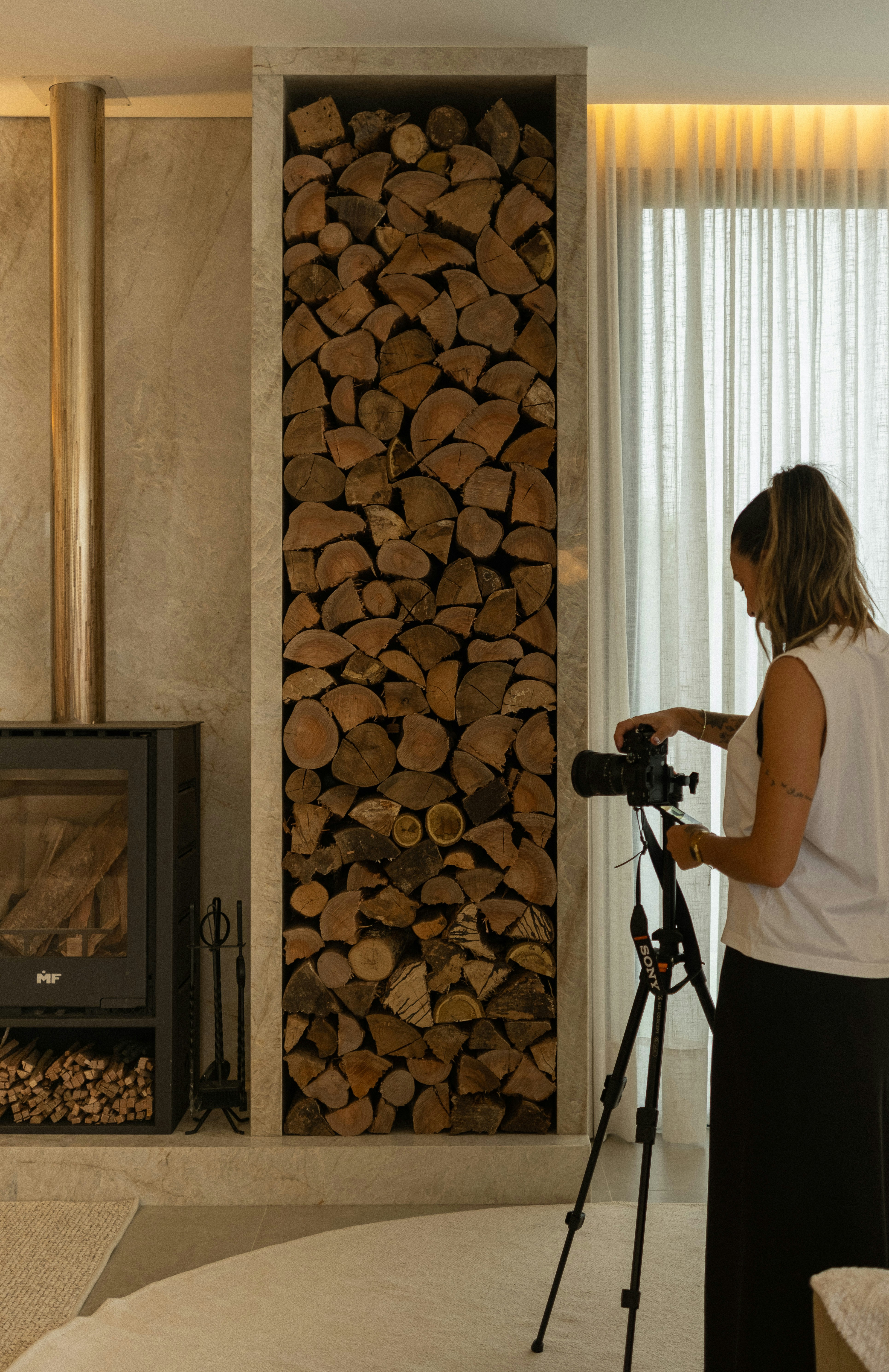 Woman filming a fireplace with stacked firewood