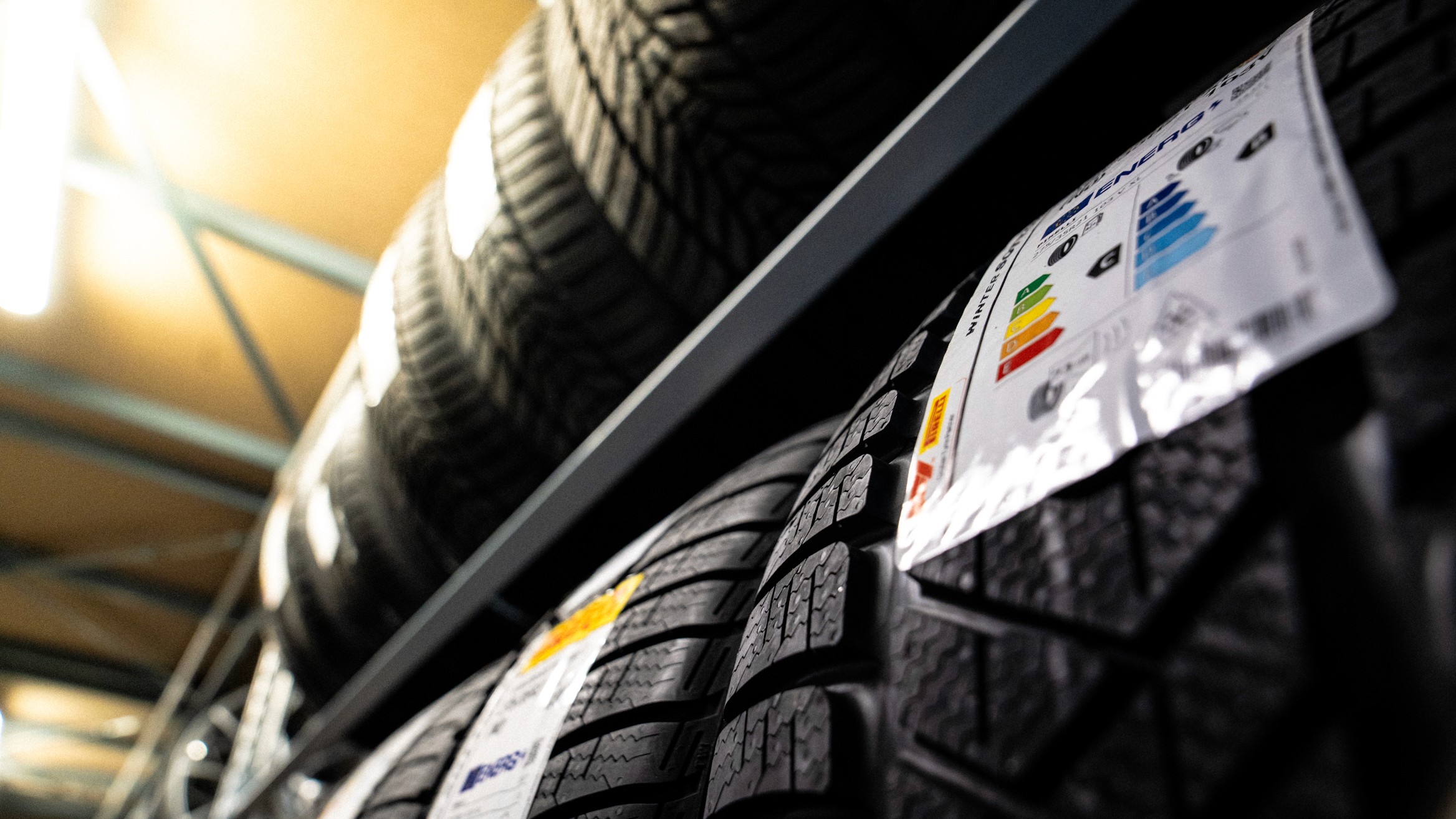 Gestapelte Autoreifen im Lagerregal, teilweise mit EU-Energielabels versehen, die Informationen zu Rollwiderstand, Nasshaftung und Geräuschpegel zeigen. Die Aufnahme ist aus der Froschperspektive fotografiert und vermittelt einen professionellen Eindruck eines Reifenlagers.