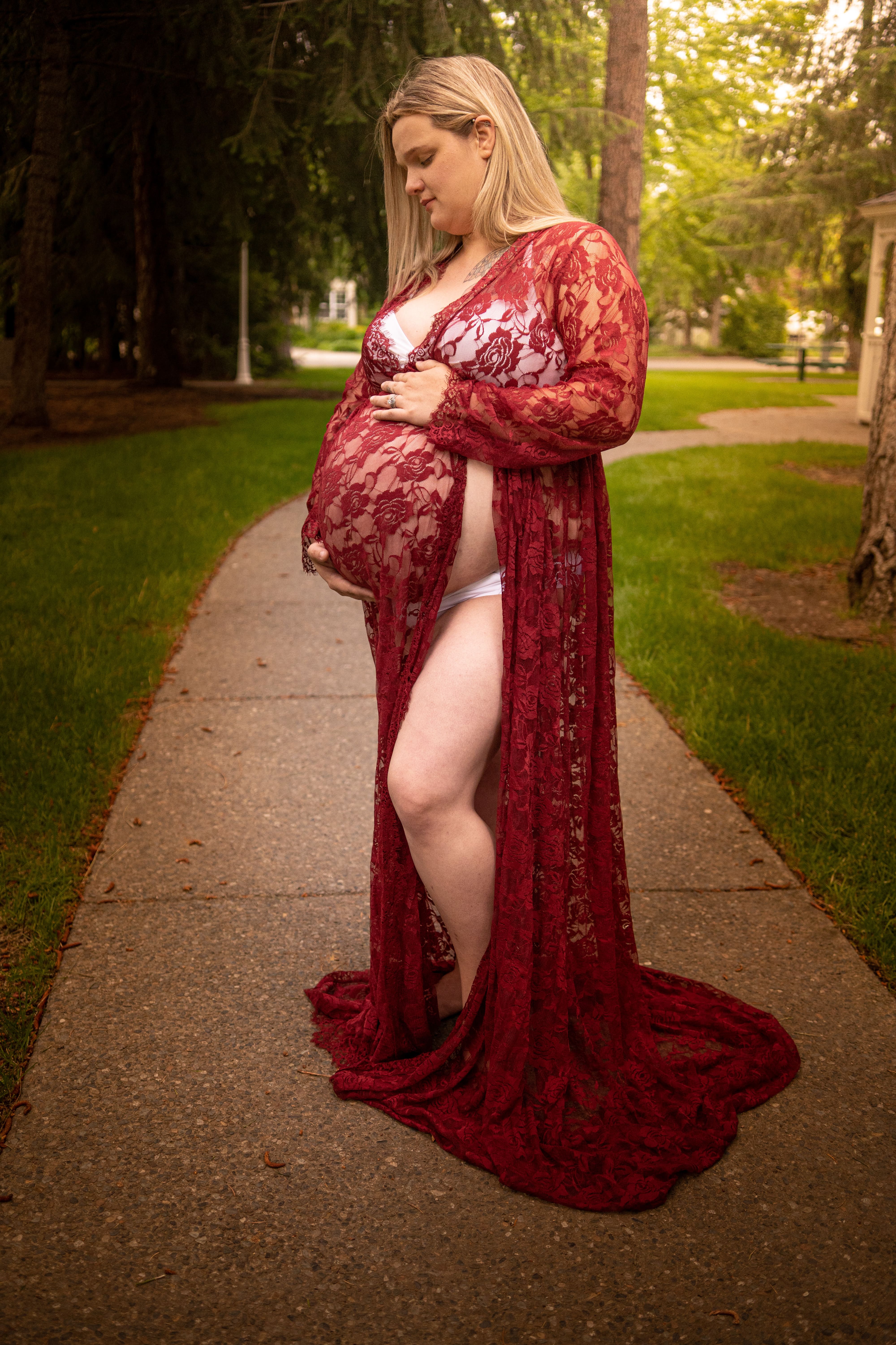 A pregnant woman with a red dress standing on a concrete path