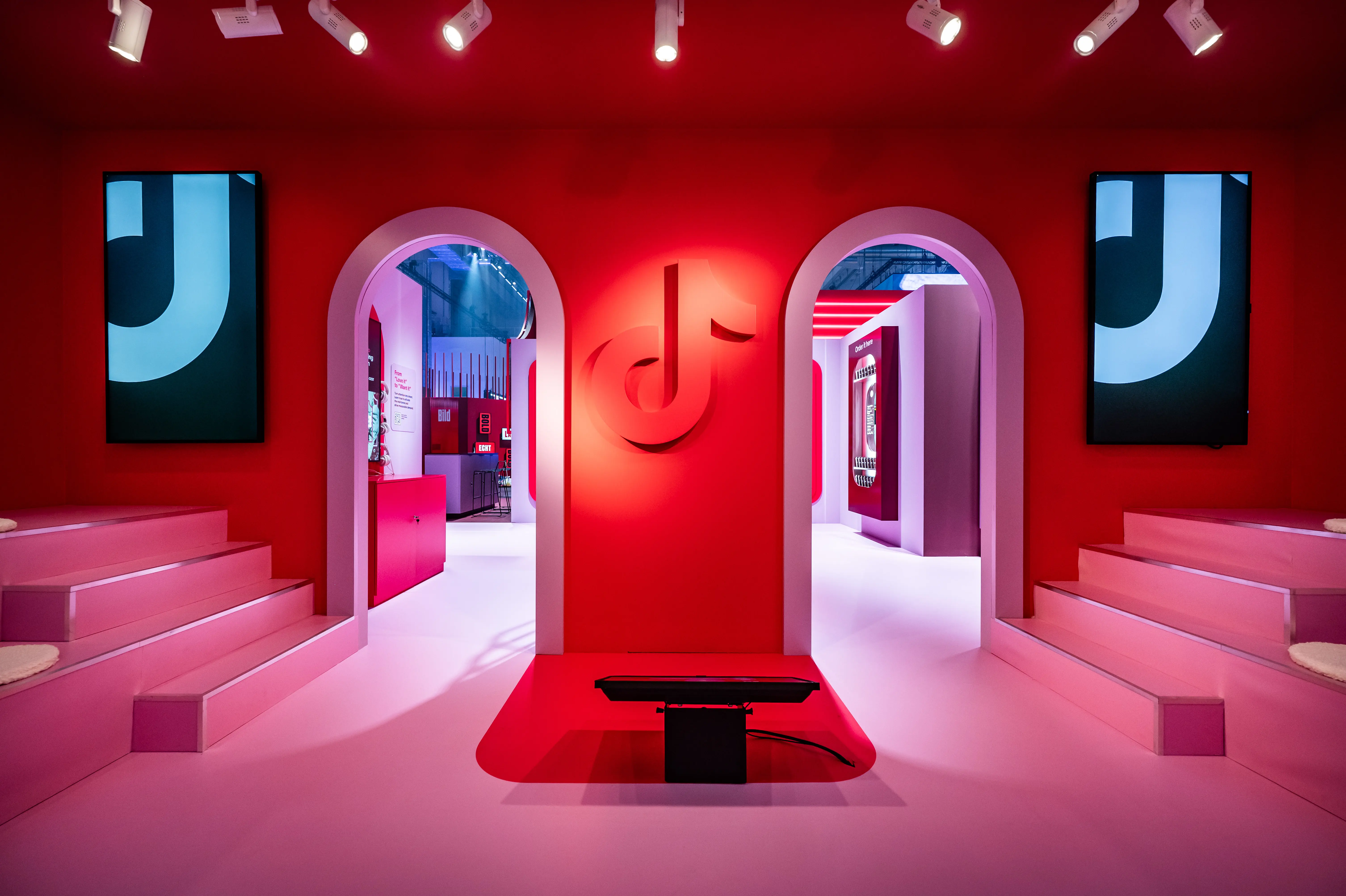 Red booth interior with TikTok logo between two arches, pink tiered seating and screens.