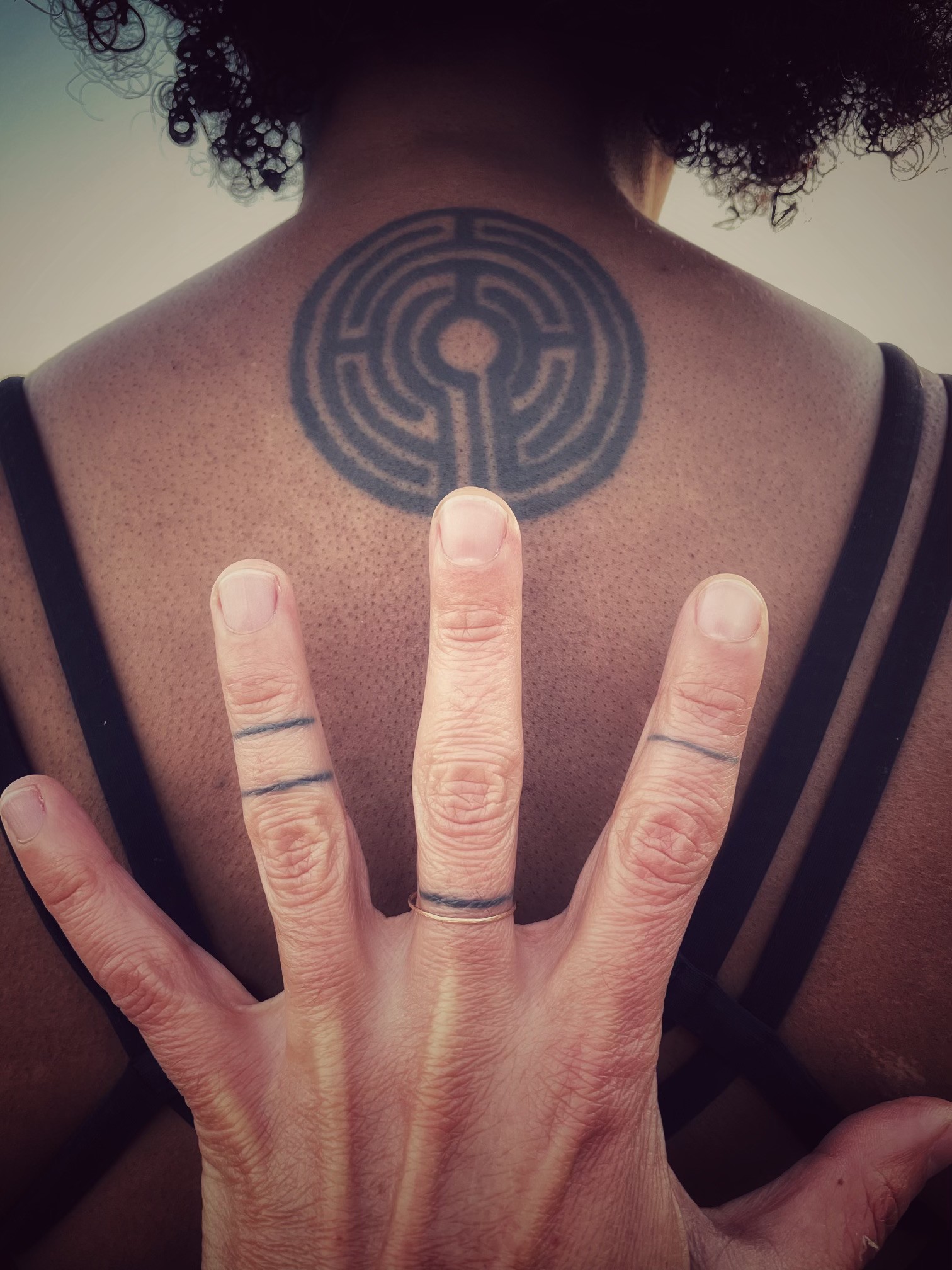 A person with curly hair and glasses smiles at the camera, seated in a cozy workspace with warm lighting.
