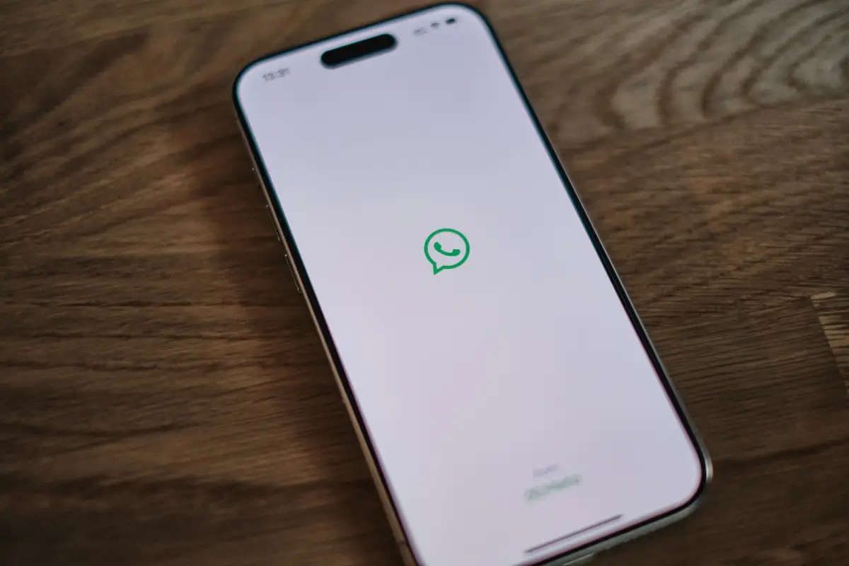 나무 테이블 위에 놓인 스마트폰의 화면에 WhatsApp 로고가 표시되어 있습니다