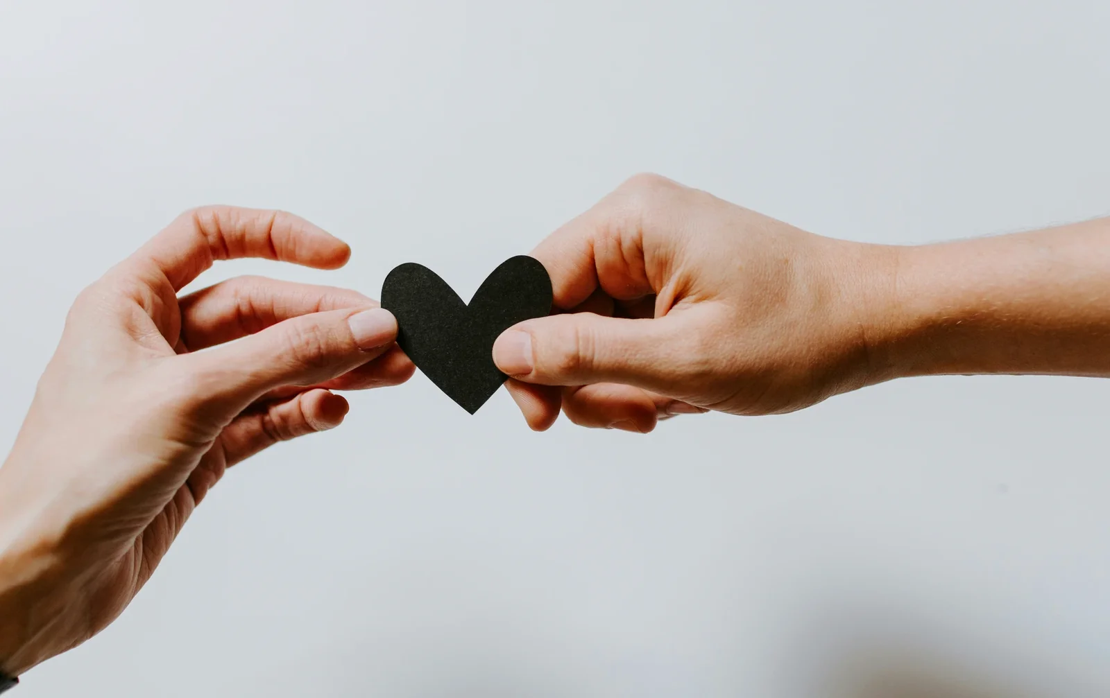 Two hands exchanging a black heart symbol against a light blue background, representing shared values and connection.