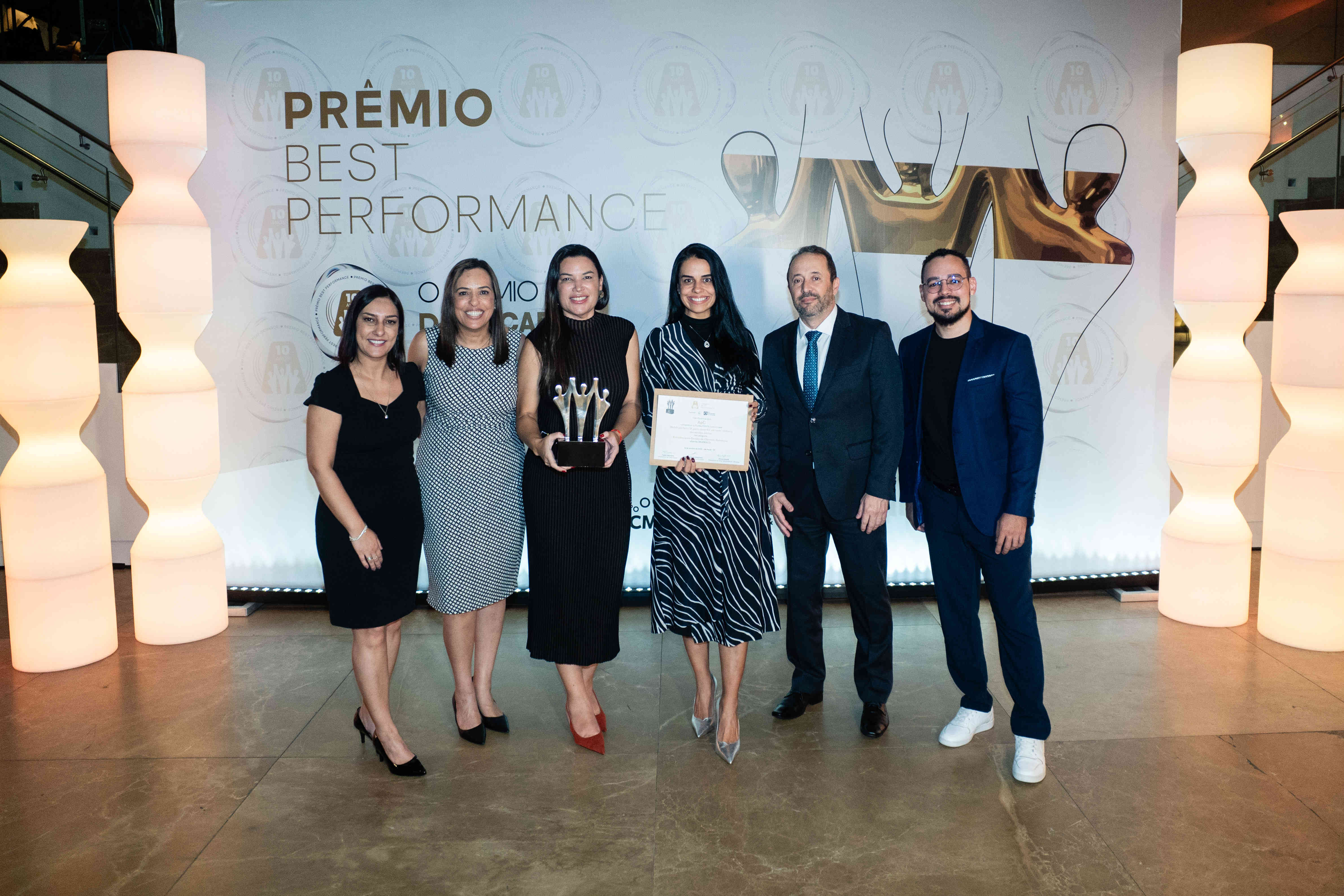 Executivos da AeC posando com troféu prata e certificado no palco do Prêmio Best Performance 2025