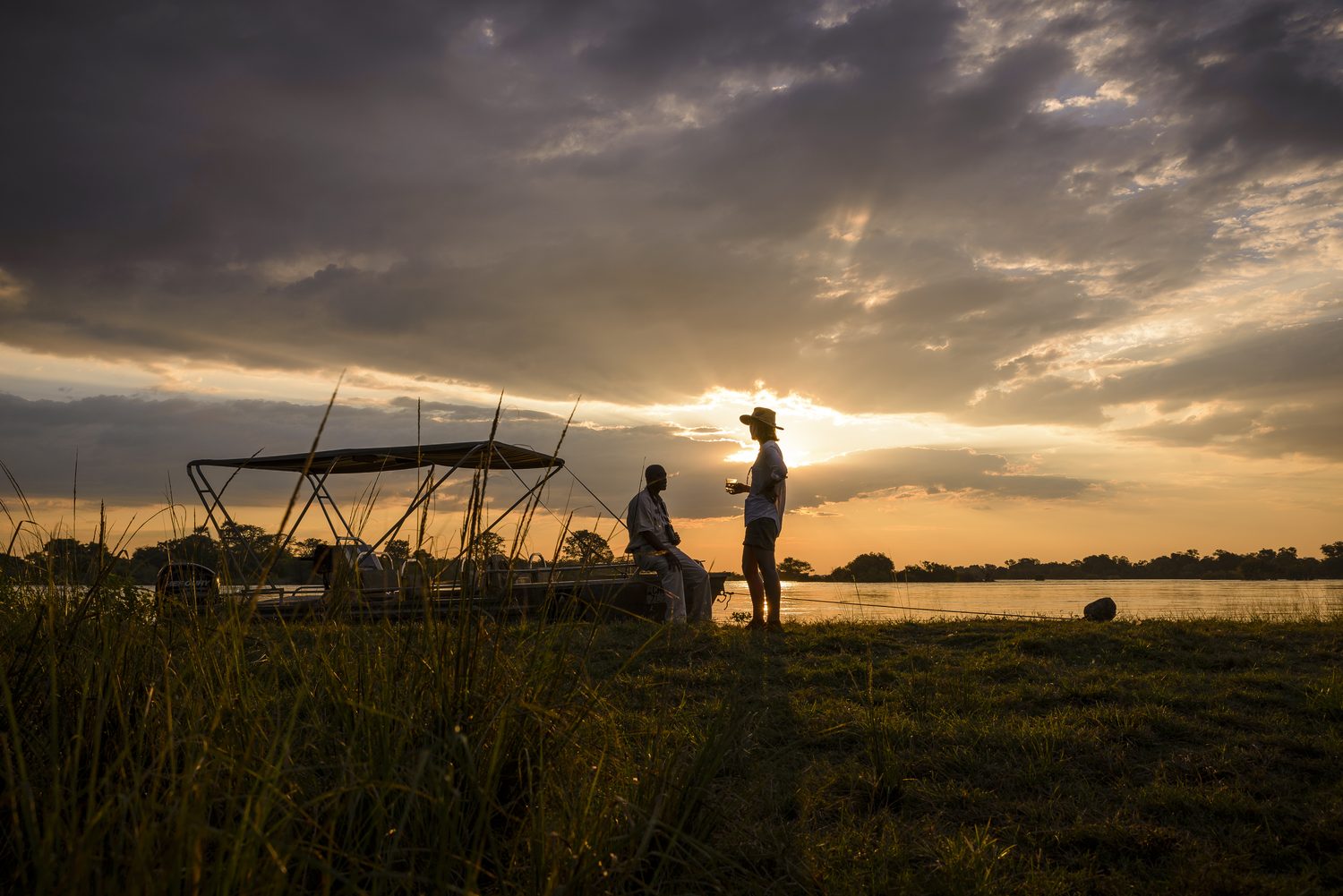 Guests sharing sundowners by the boat at a river's edge