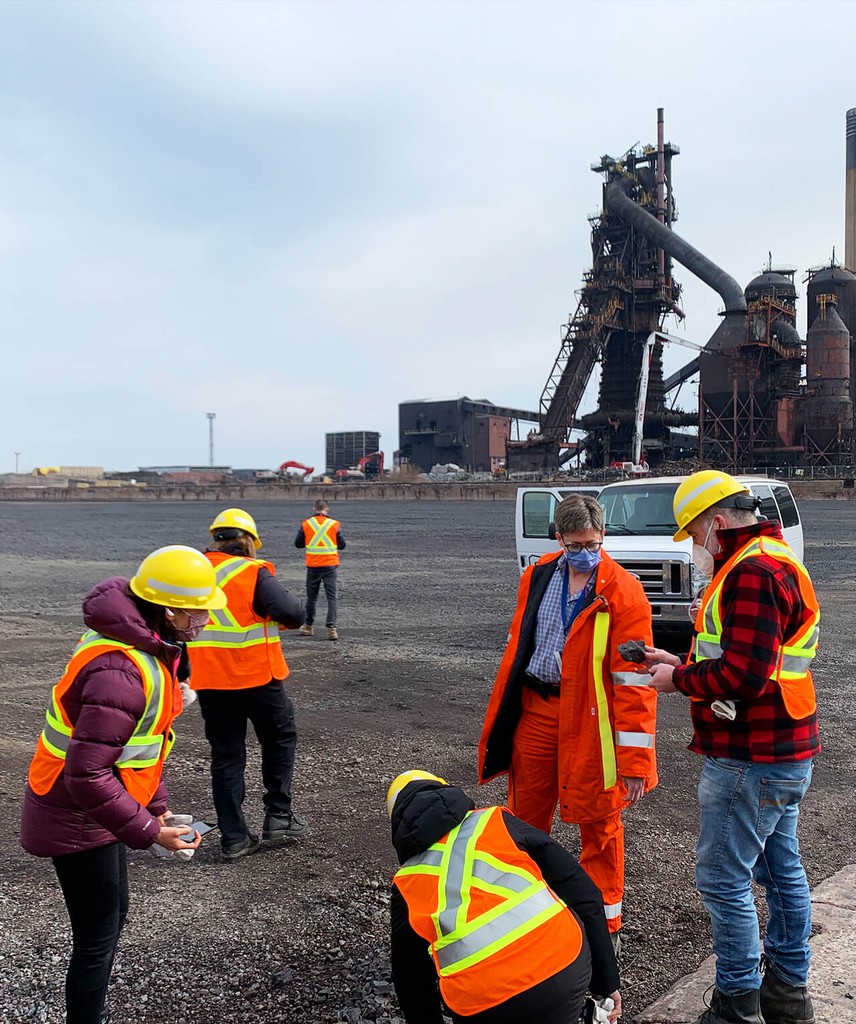 A group of people standing outside talking with each other, with Steelport visible in the distance.