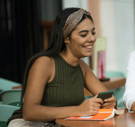 Femme utilisant son téléphone à une table, gestion d’épargne sur application mobile