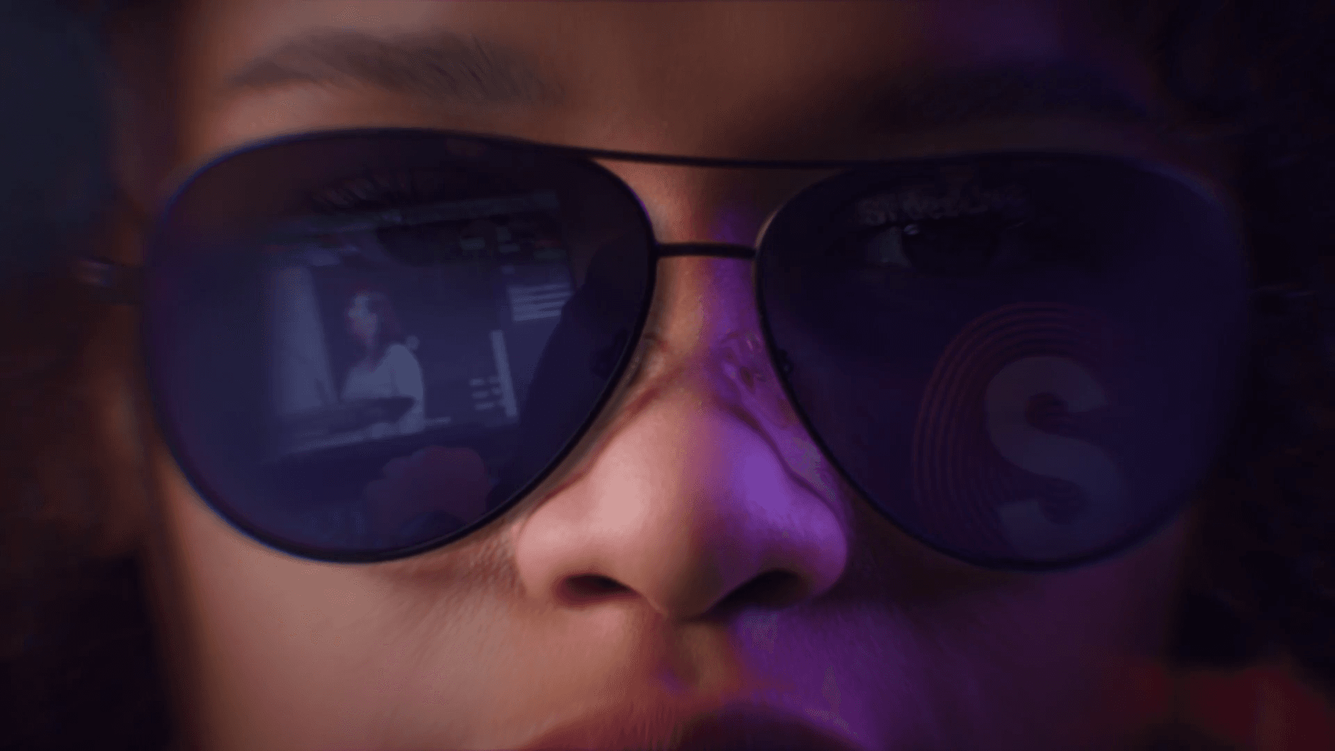 Close-up of a girl wearing glasses, with a SlidesLive technician reflected in the background.