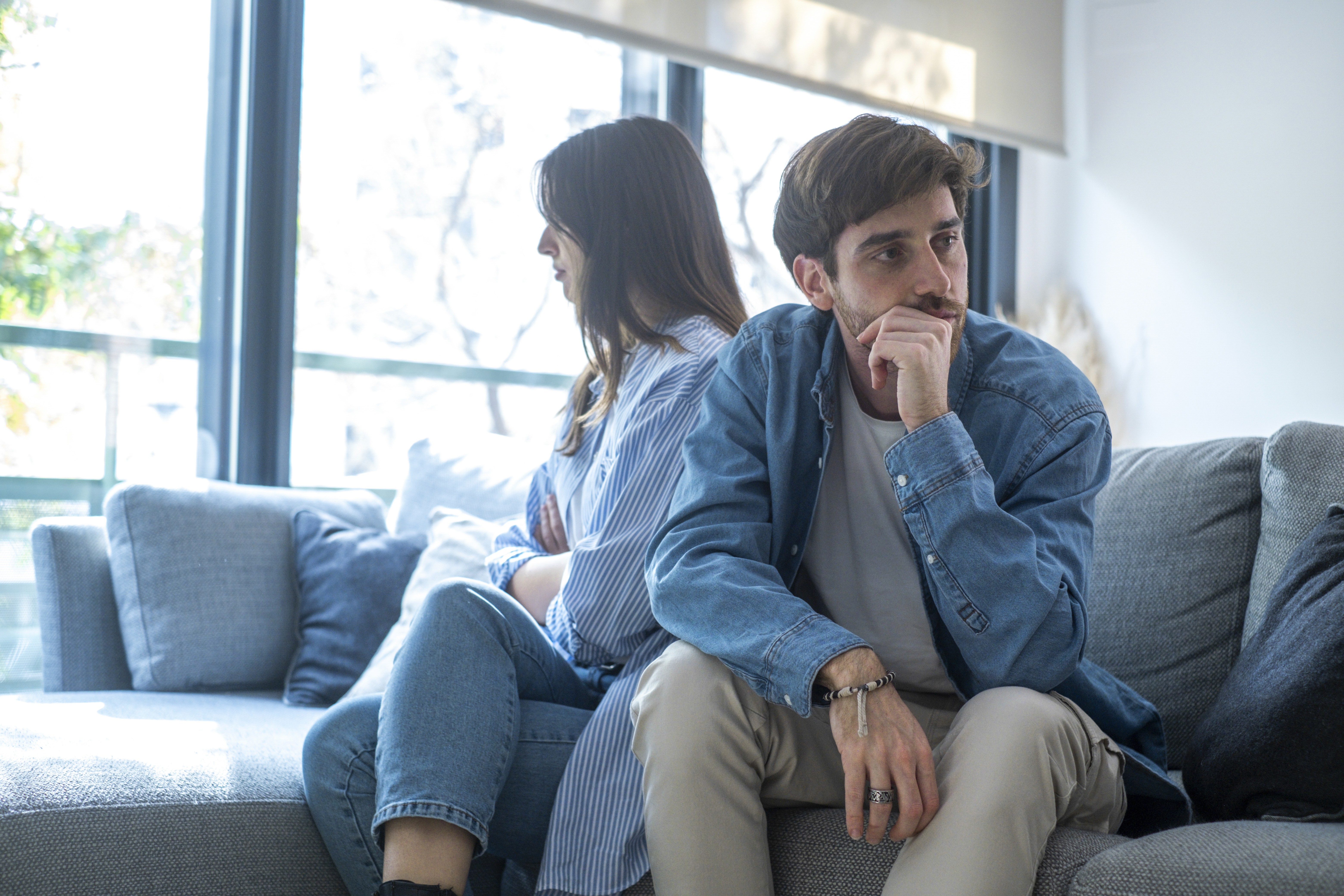 Couple sitting apart on a couch looking stressed and distant, representing marital conflict and the consideration of mediation as an alternative to contested divorce in Massachusetts