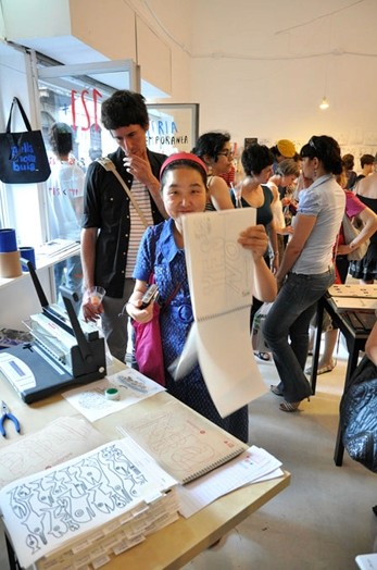 A photo of a woman with a sketchbook in a library full of people.