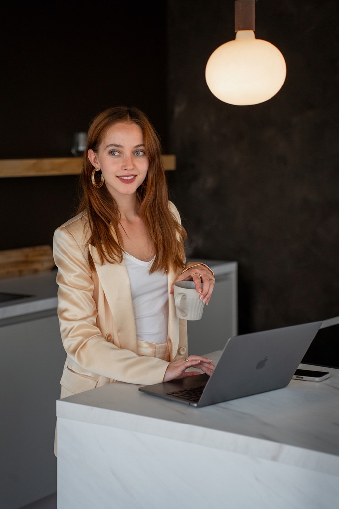 FRWD socials. Kirsten Magdalena Bijl aan een aanrecht met haar laptop. Werken in een geel pak. Kop thee in hand.