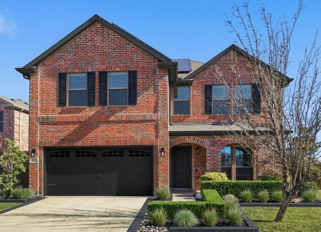 Brick house exterior update — black carriage garage door, dark trim, structured landscaping on red brick