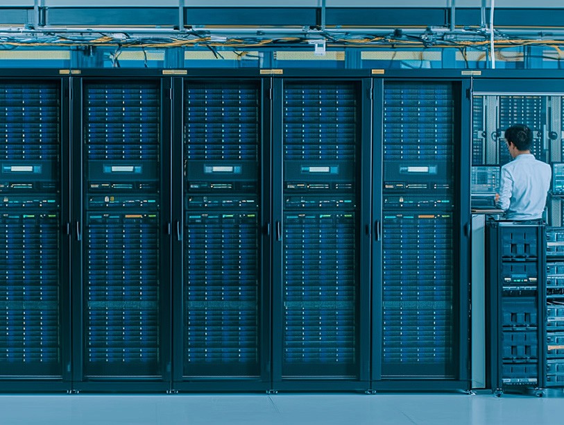 A technician examines servers in a modern data center, featuring multiple racks filled with network equipment, cables, and blinking indicator lights, illustrating the complexities of data management and information technology infrastructure.